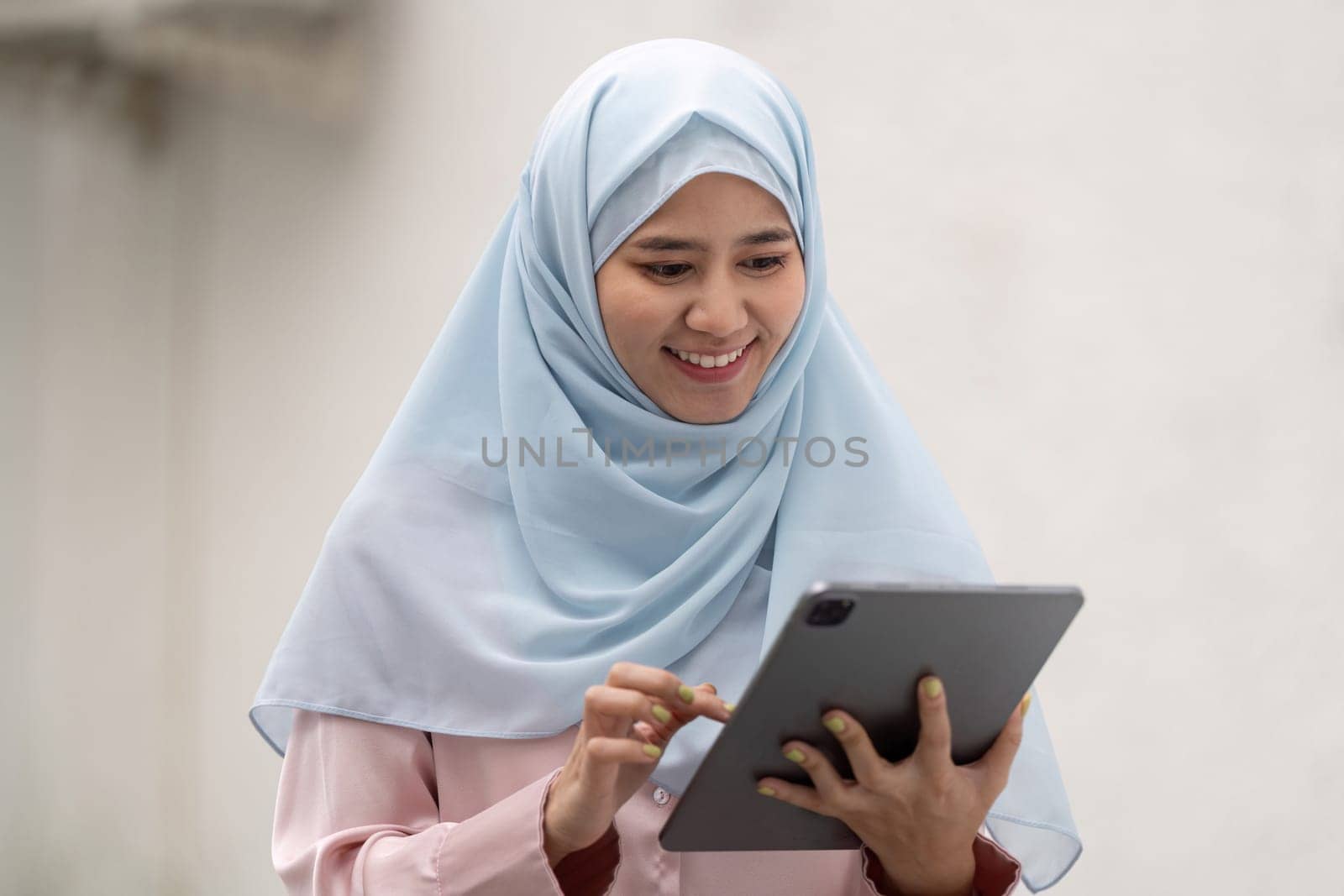 A Muslim businesswoman wearing a hijab, happily using a tablet outdoors and engaging with digital content.