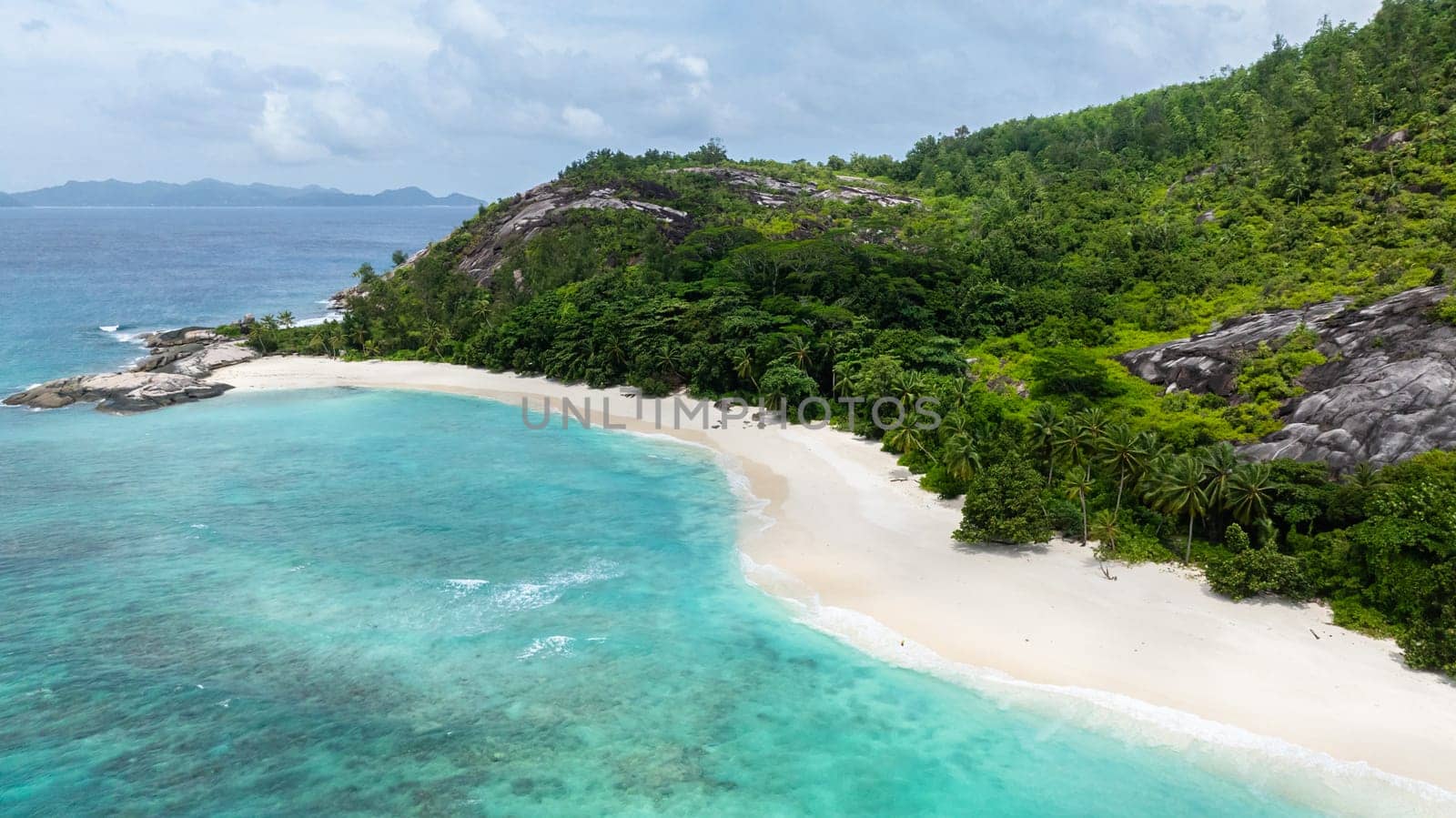 A tranquil beach with soft white sand and lush, vibrant tropical vegetation. Seychelles, Therese island.