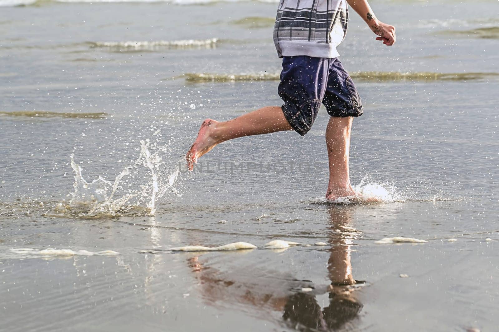 Boy runs along beach and makes splashes in the water at Pacific Beach in Washington.