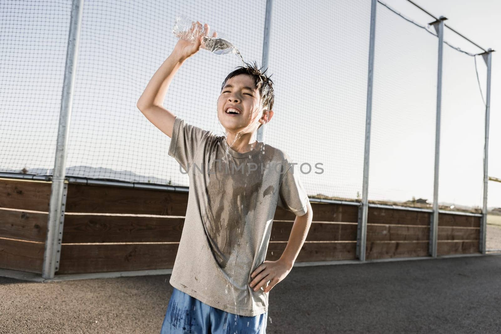 A boy exhausted after a hard practice pours cool water over his head.