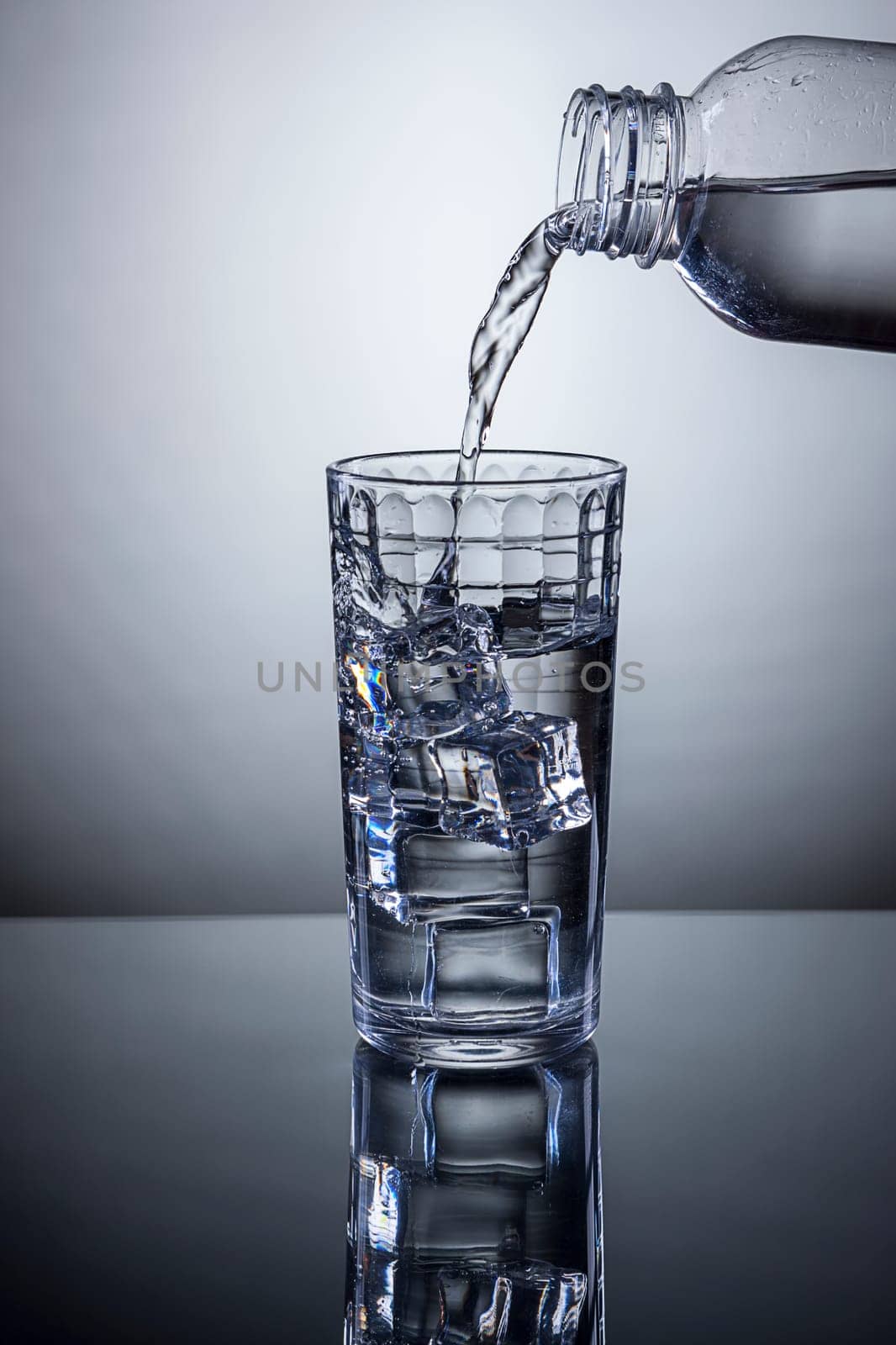 Water being poured from a bottle into a glass of ice.