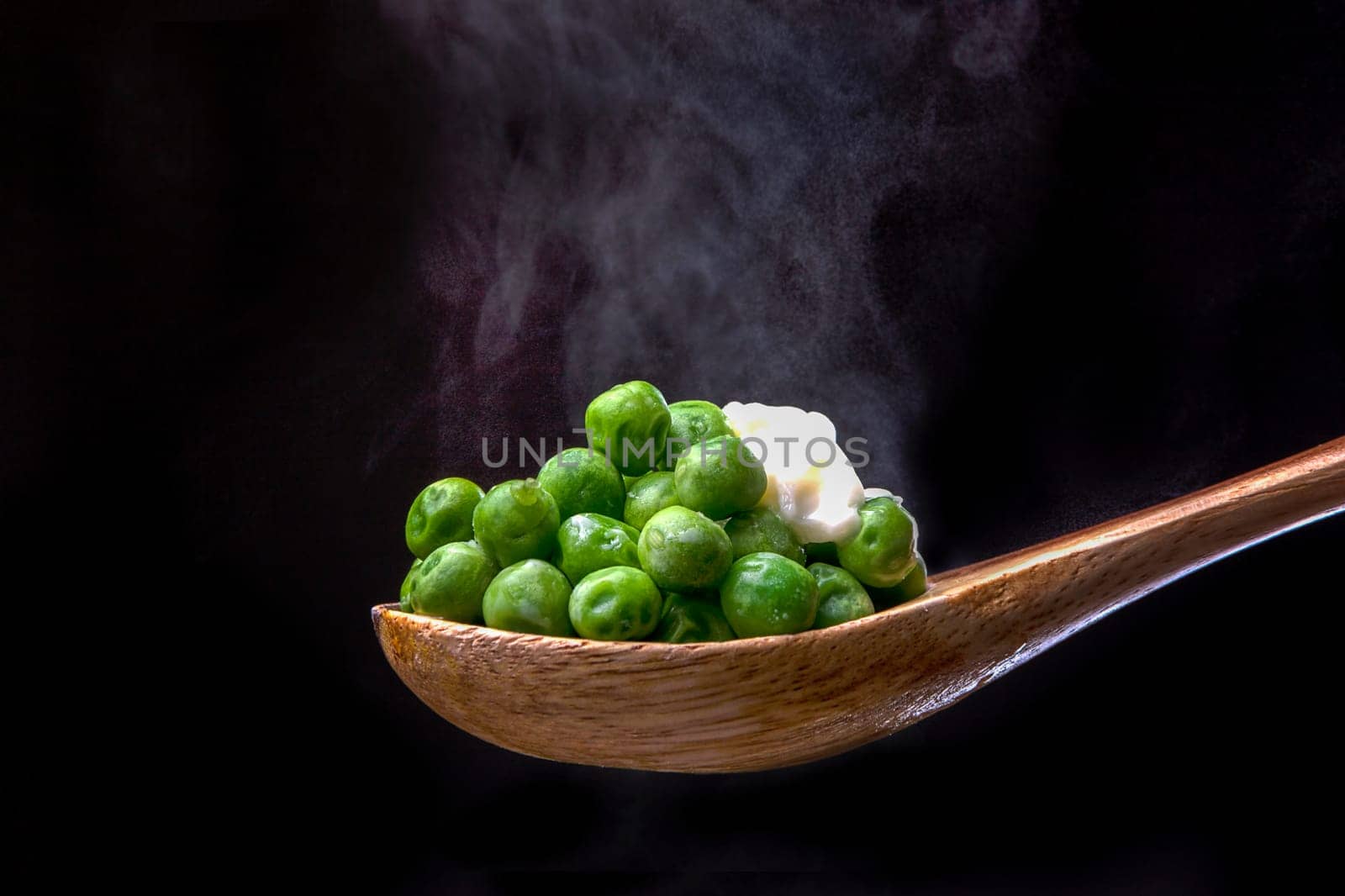Peas topped with butter on a wooden spoon with steam from below.