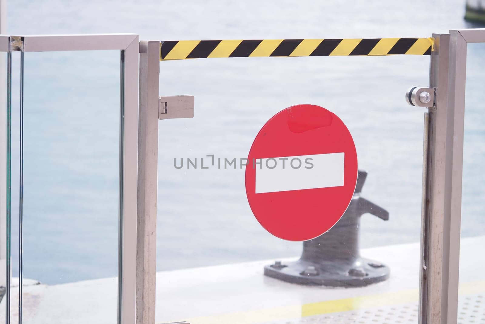 A no entry sign is displayed on a gate at a coastal harbor setting.