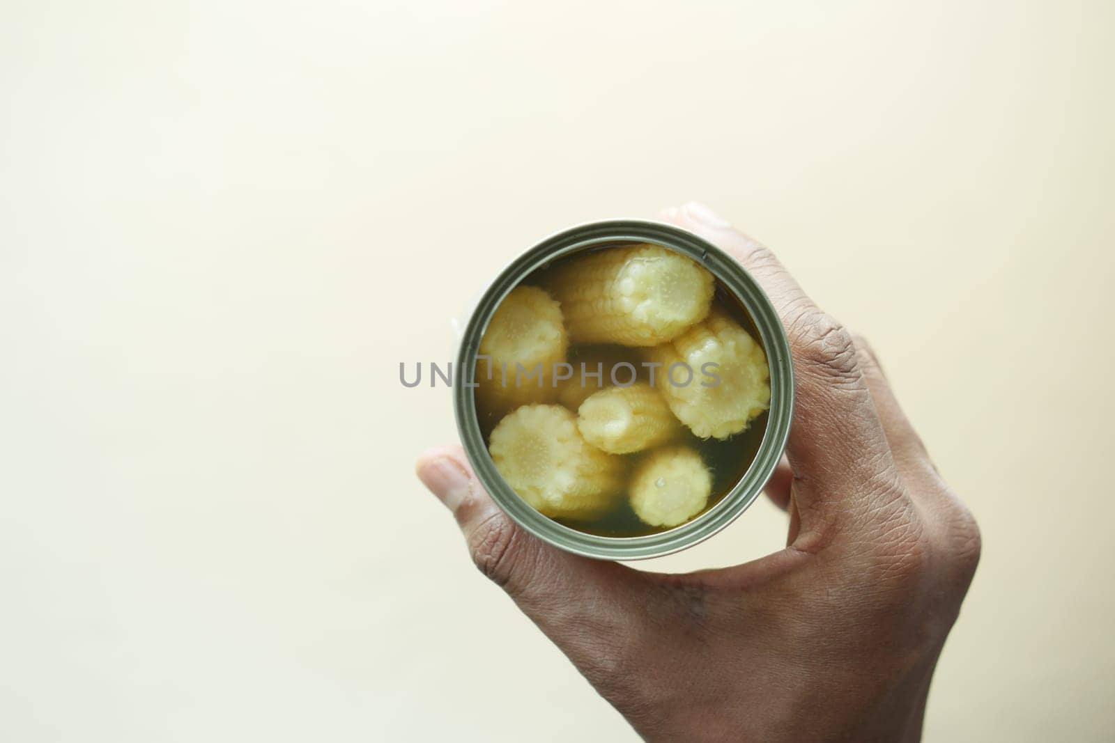 A person holds a jar filled with baby corn submerged in liquid.
