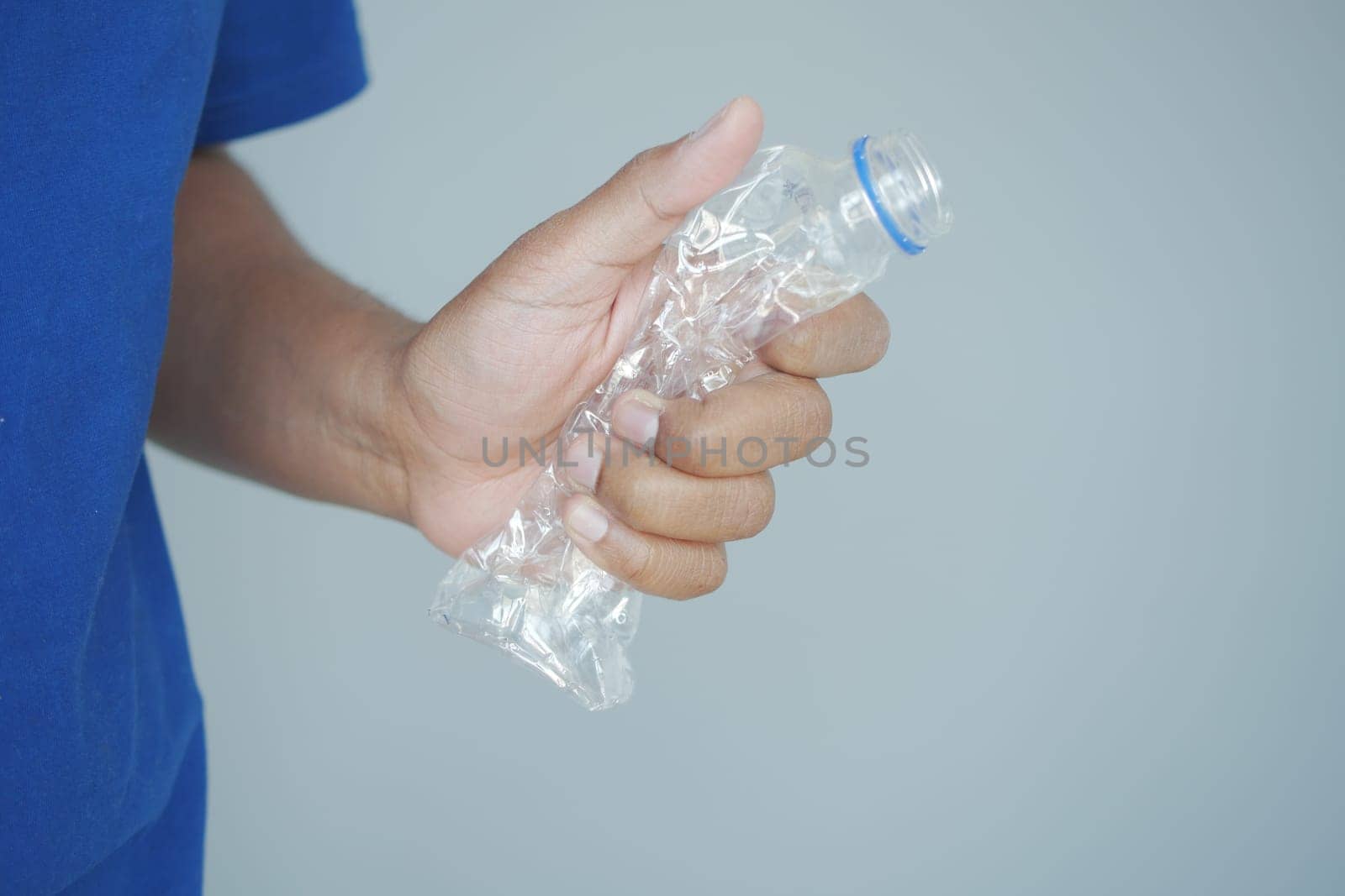 Crushed plastic water bottle held in a person's hand, indoors.