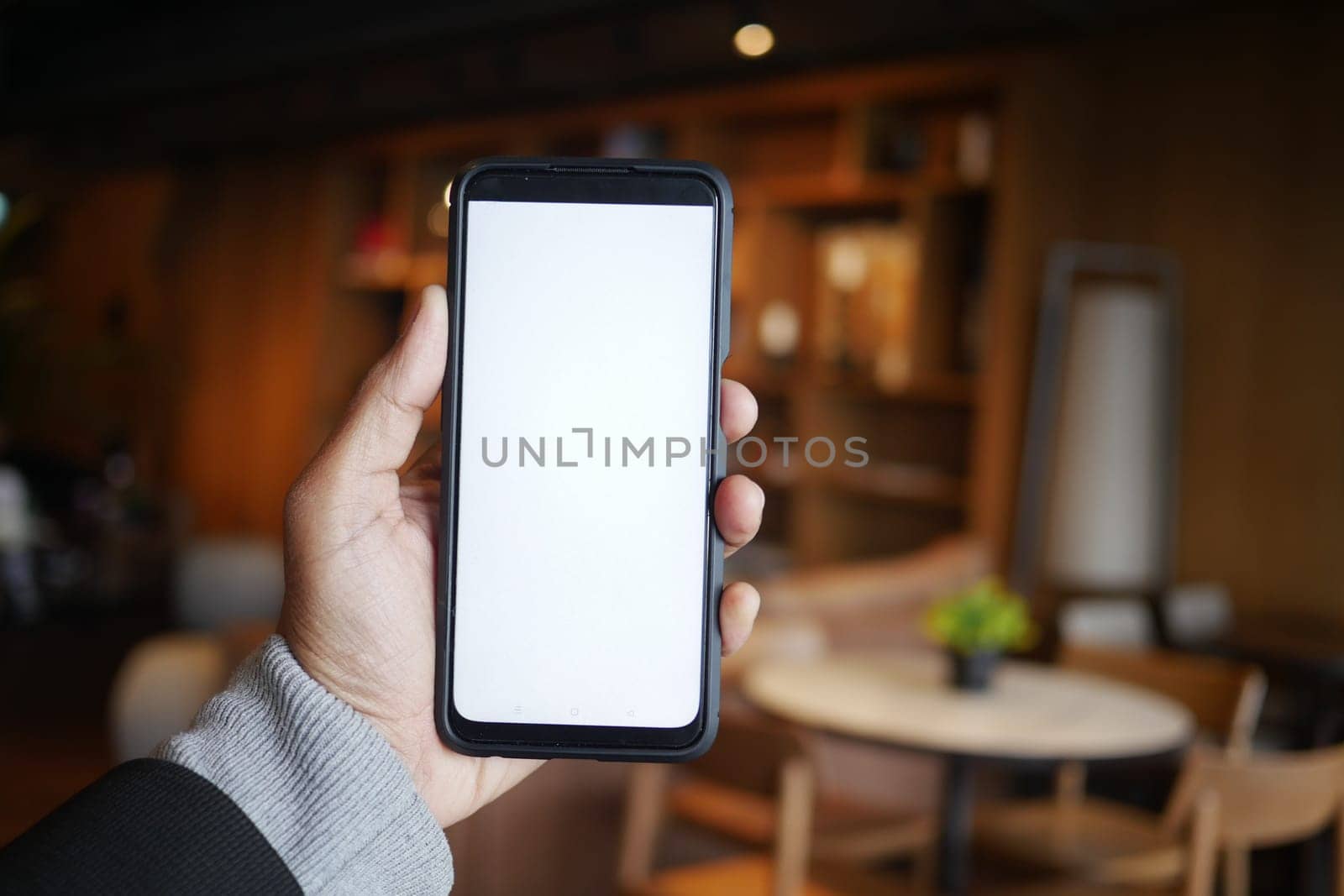 A person presents a smartphone with a blank screen in a stylish cafe.