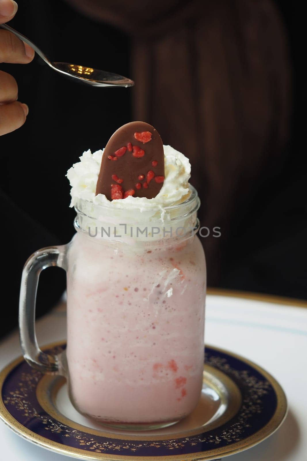 A hand adds a spoonful of chocolate to the creamy dessert drink.