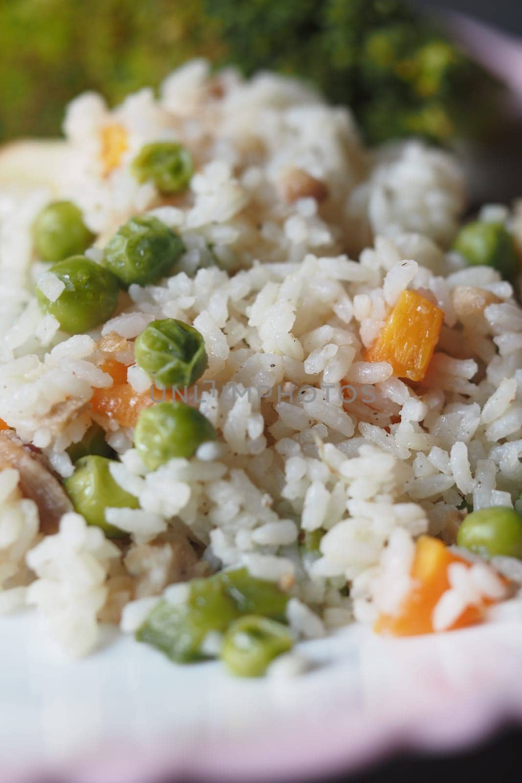 A vibrant dish of rice mixed with peas and carrots garnished with greens.