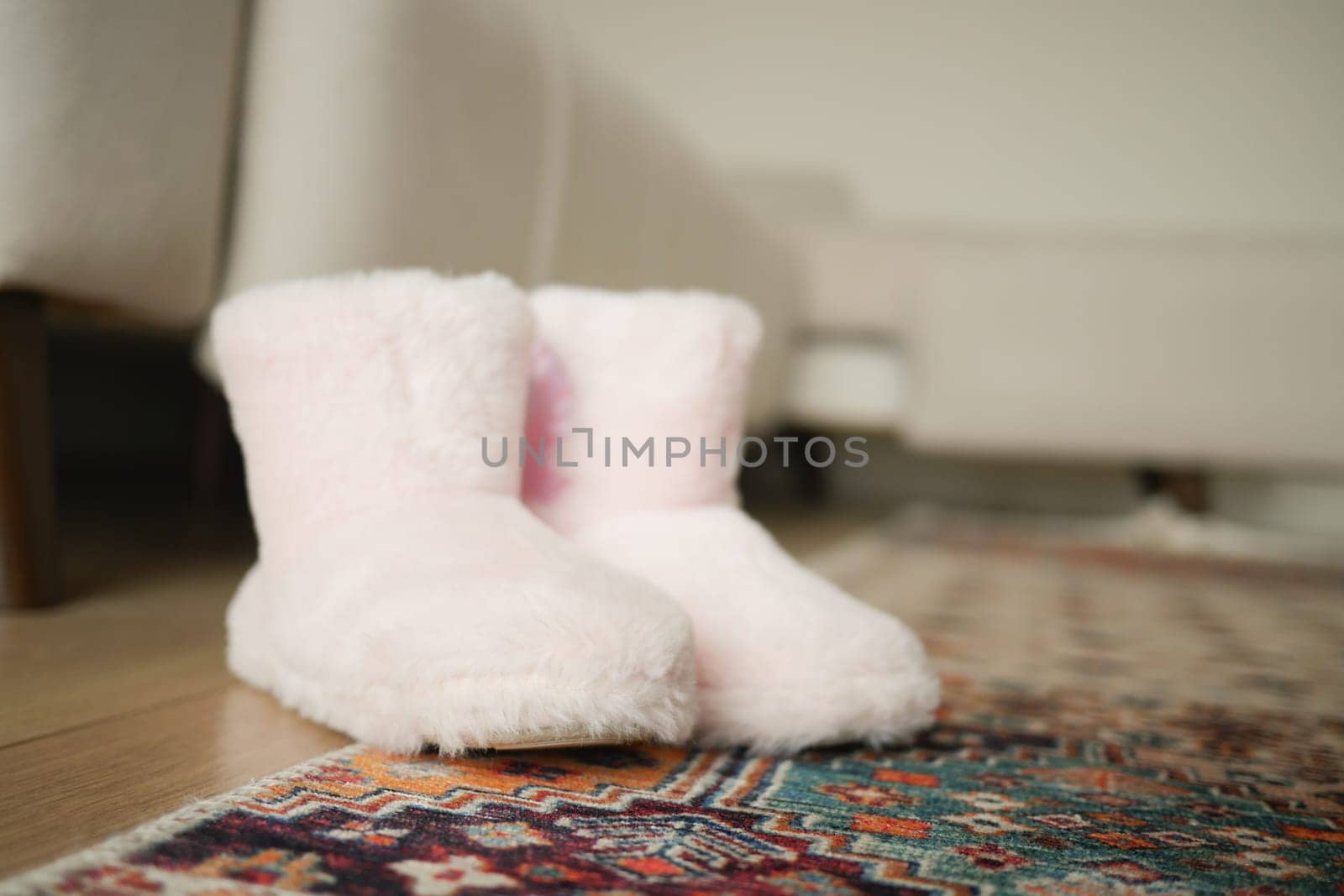Soft pink slippers are placed neatly on a colorful rug indoors.