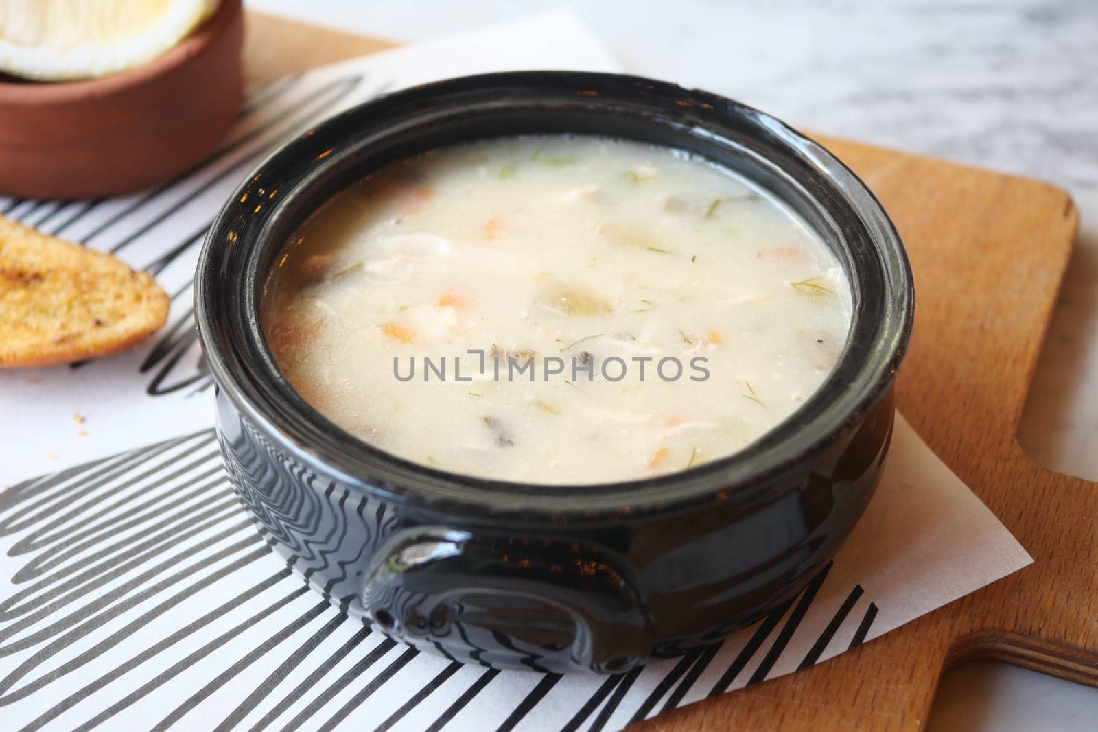 Warm chicken soup with vegetables in a black bowl beside toasted bread.