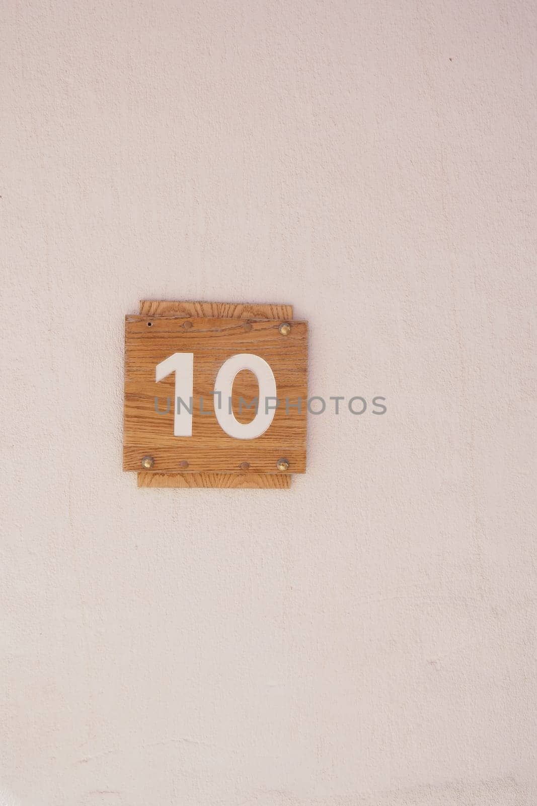 Wooden number 10 sign attached to a plain wall, minimalistic style.