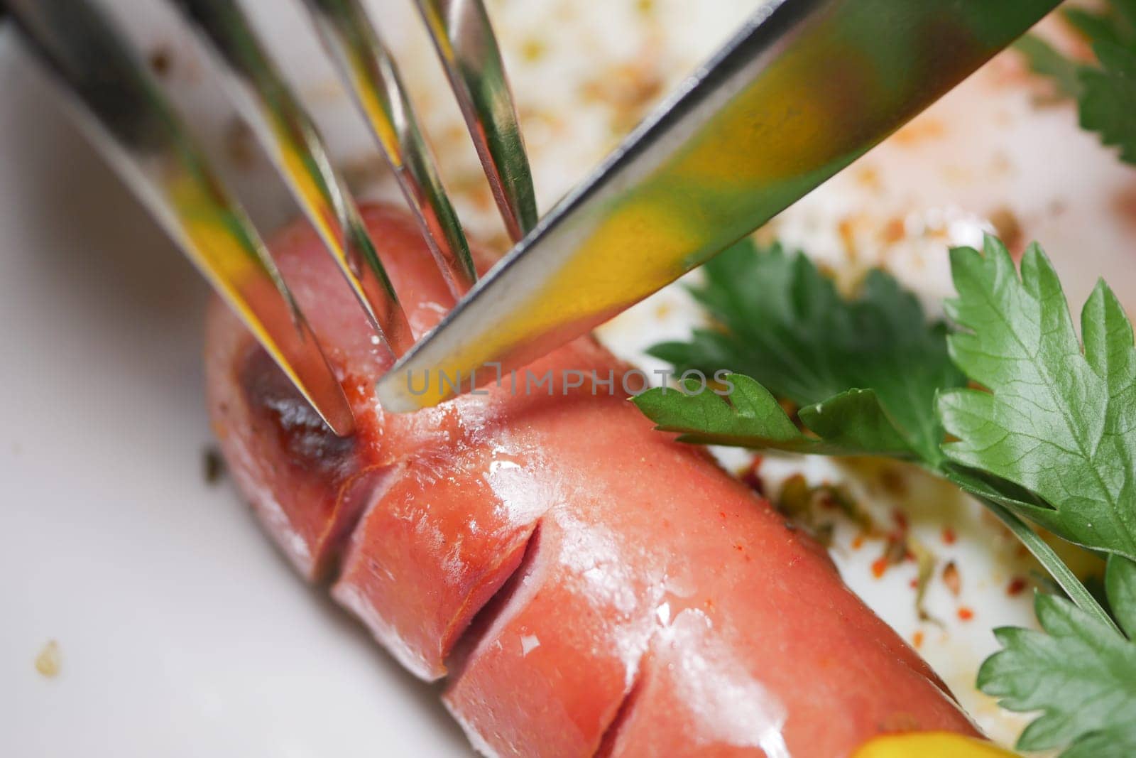 A close-up of a fork and knife slicing through a sausage with herbs.