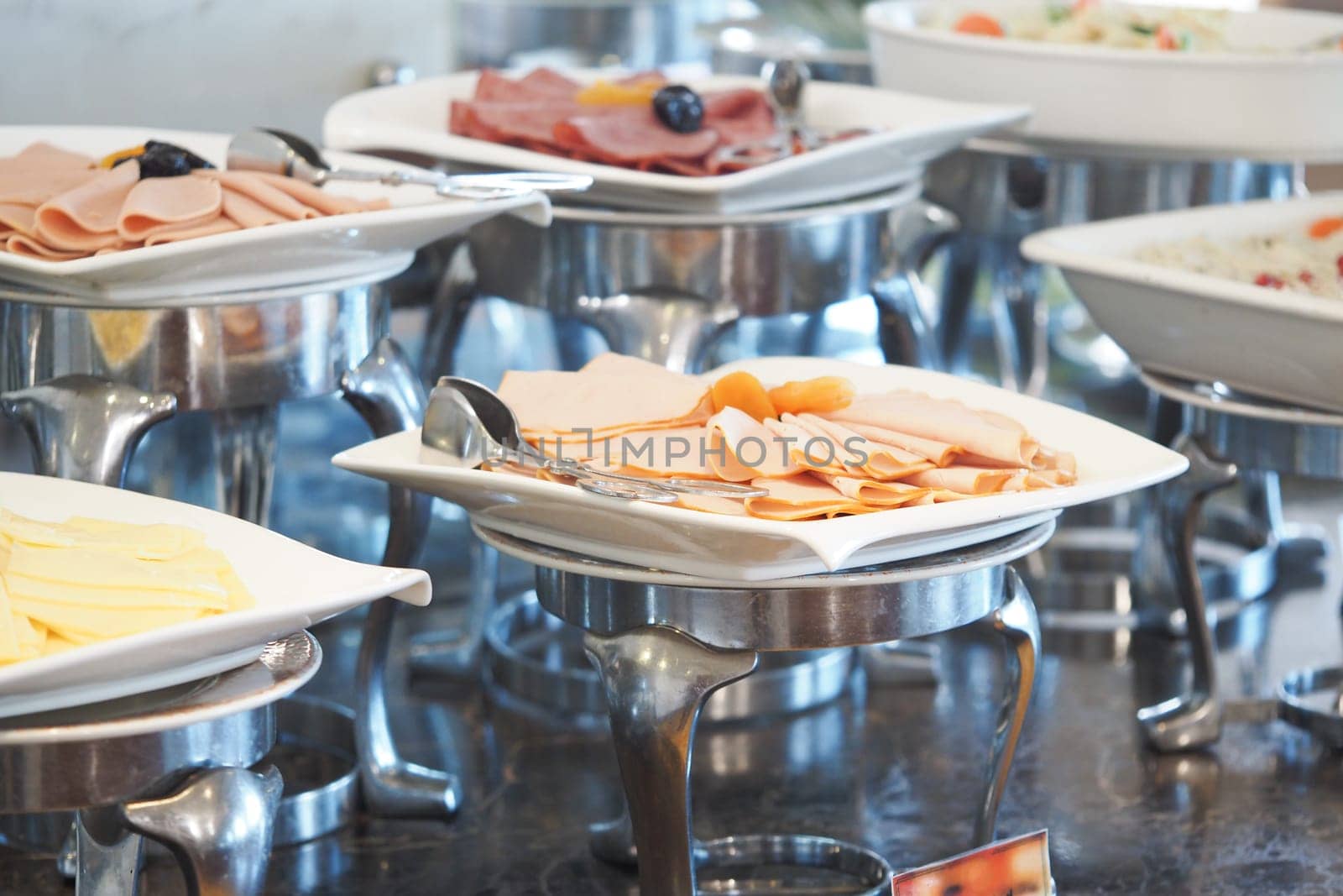 Several plates of cold cuts and salads are arranged on a buffet table.