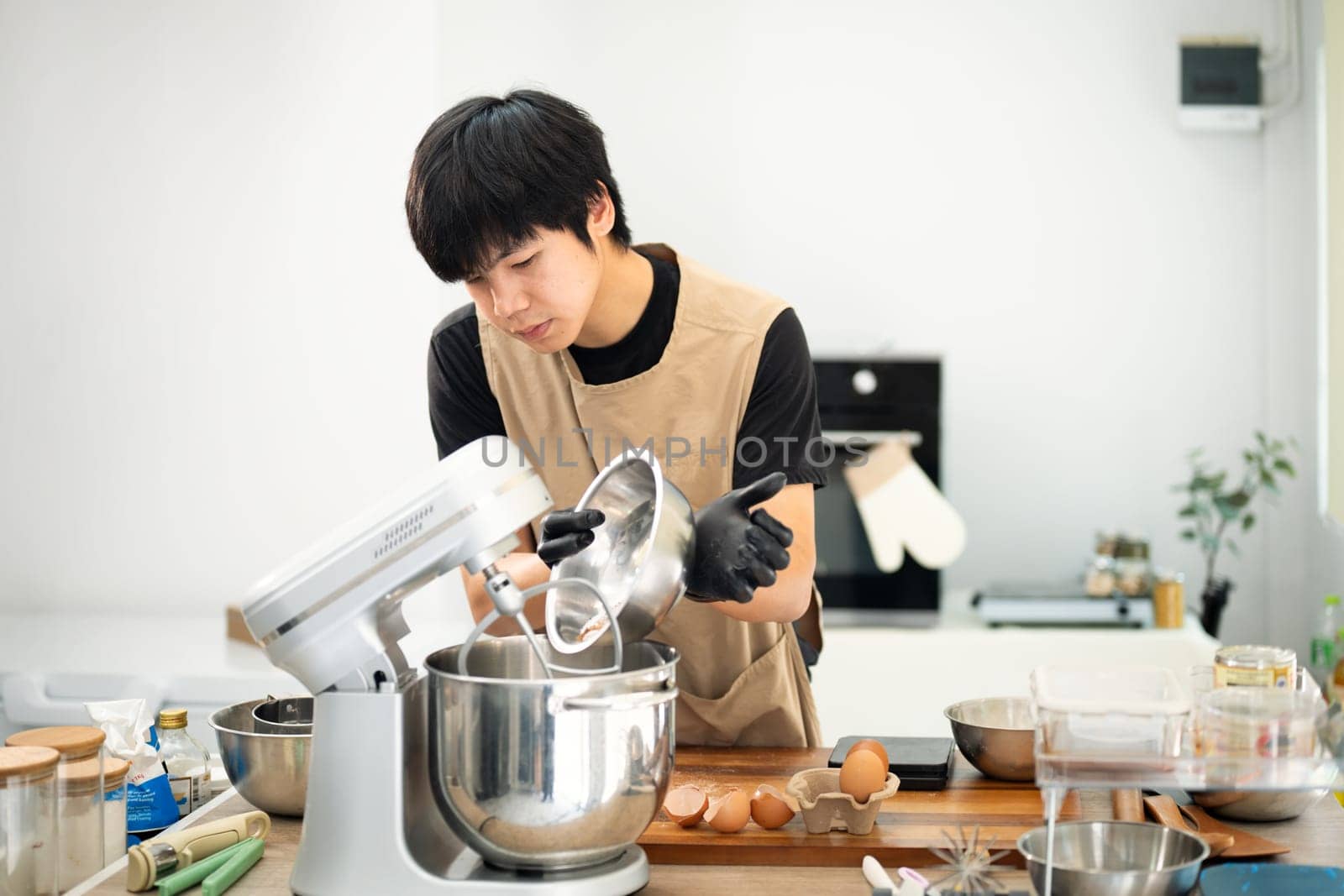 Young man adding ingredients into a stand mixer while preparing cookie dough.