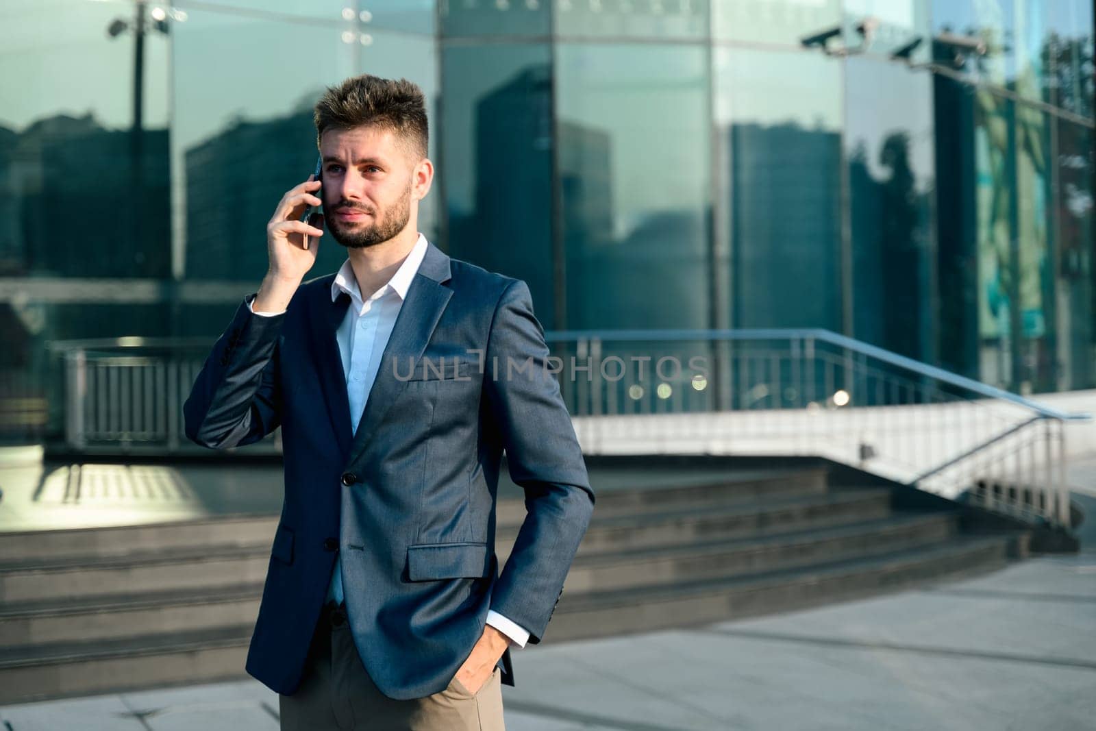 Bearded businessman talking on mobile phone outside office building.