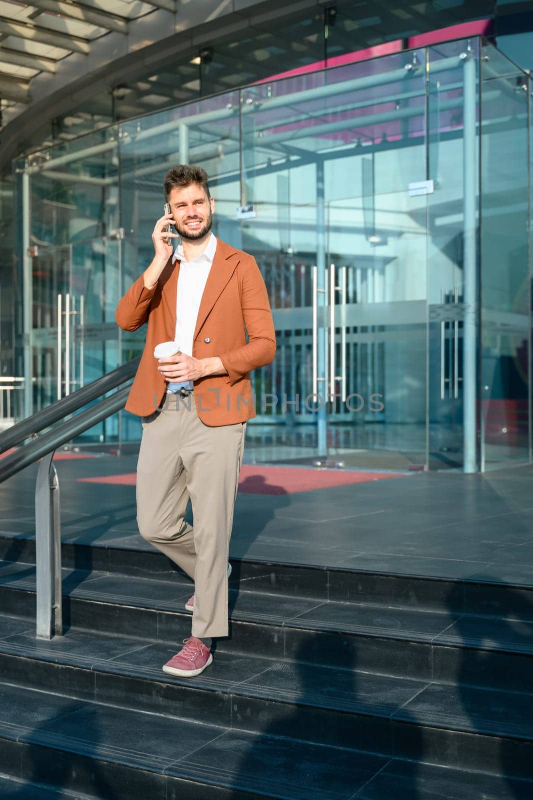 Stylish businessman having phone conversation while walking out of office building.