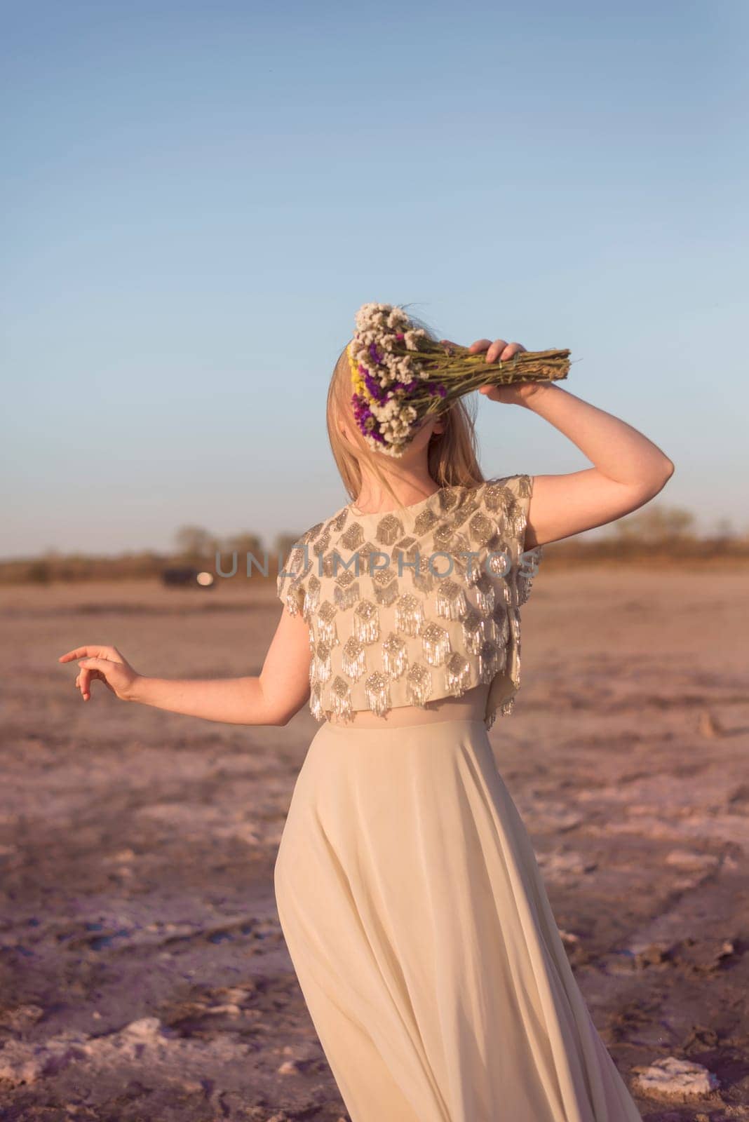blonde girl stands in the middle of a salt lake. her dress flutters in the wind. the surface of the shore is pink. she has a bouquet in her hands, she covers her face. kuyalnik, odessa