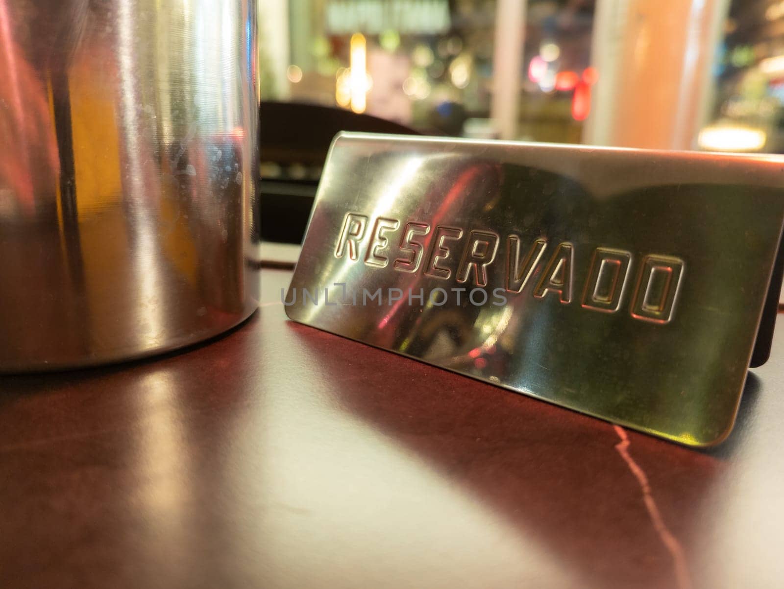 A close-up view of a metal reservado sign placed on a table, suggesting a reserved seating area in a vibrant restaurant or cafe atmosphere with blurred lights.