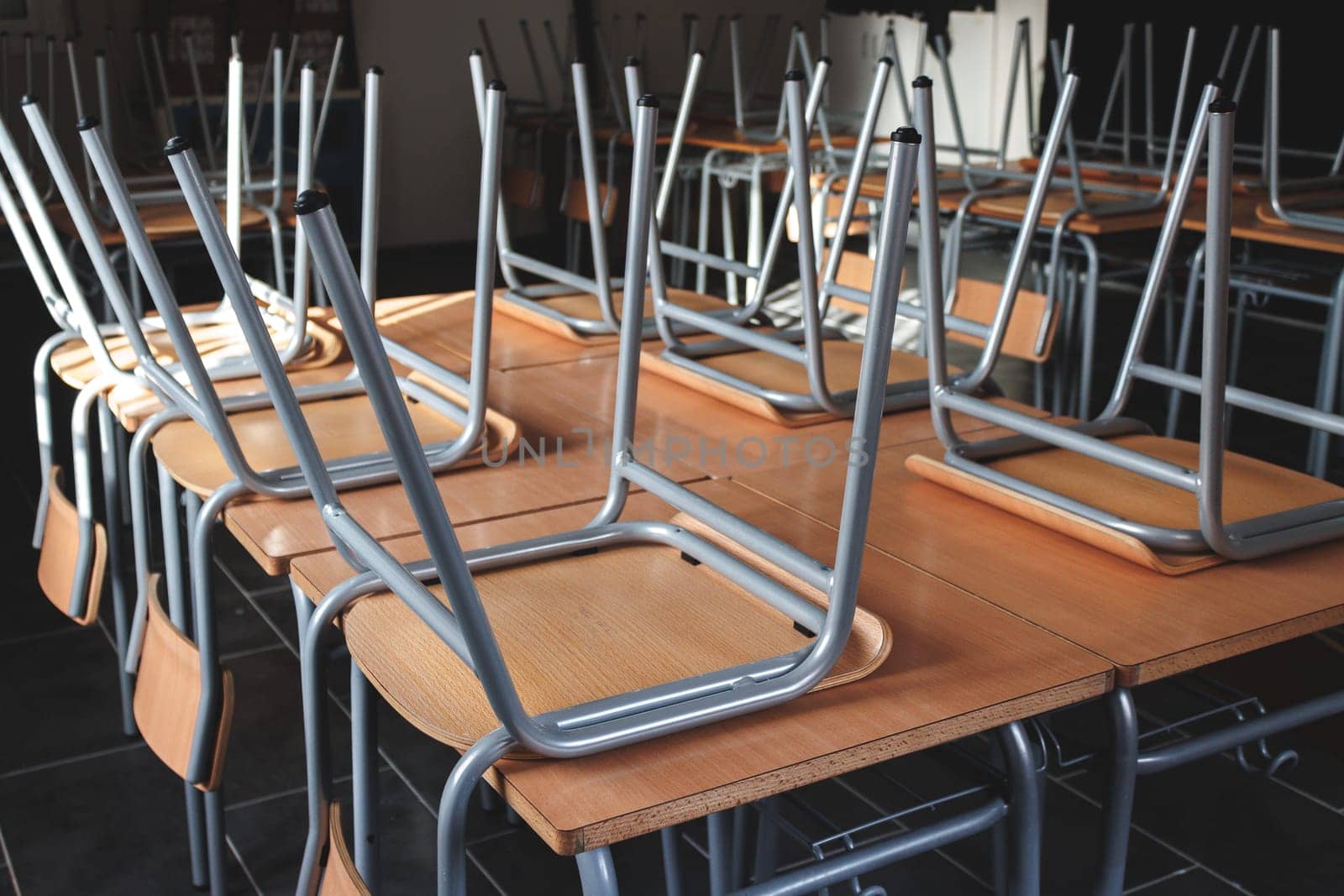 This image captures a classroom setting where chairs are stacked upside down on top of tables, creating an organized yet empty atmosphere, emphasizing a moment of silence.