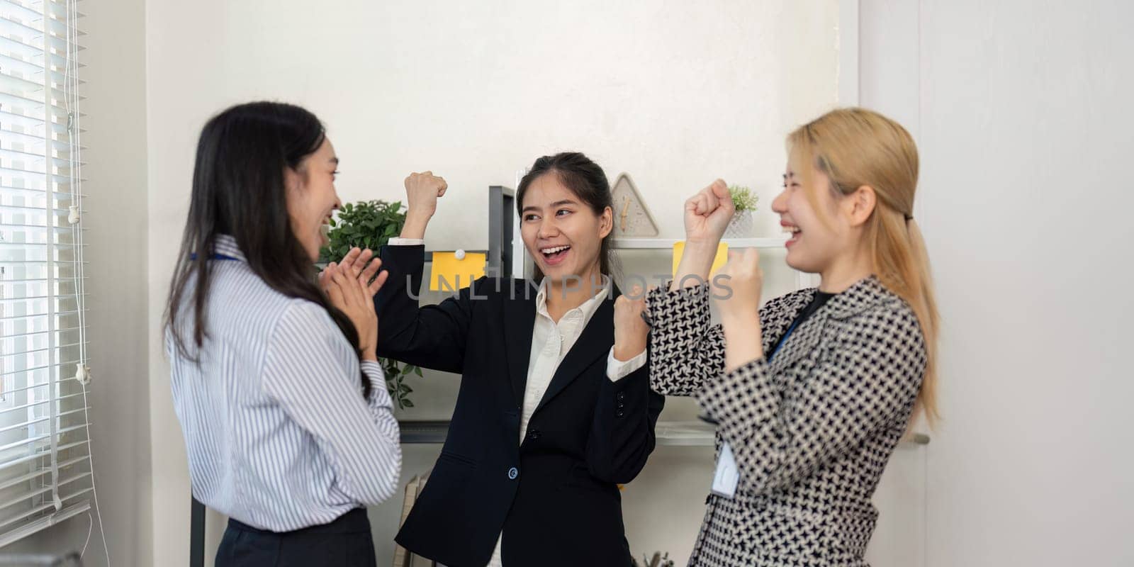 A diverse team of businesswomen expresses excitement and enthusiasm while celebrating their achievements in a modern office.