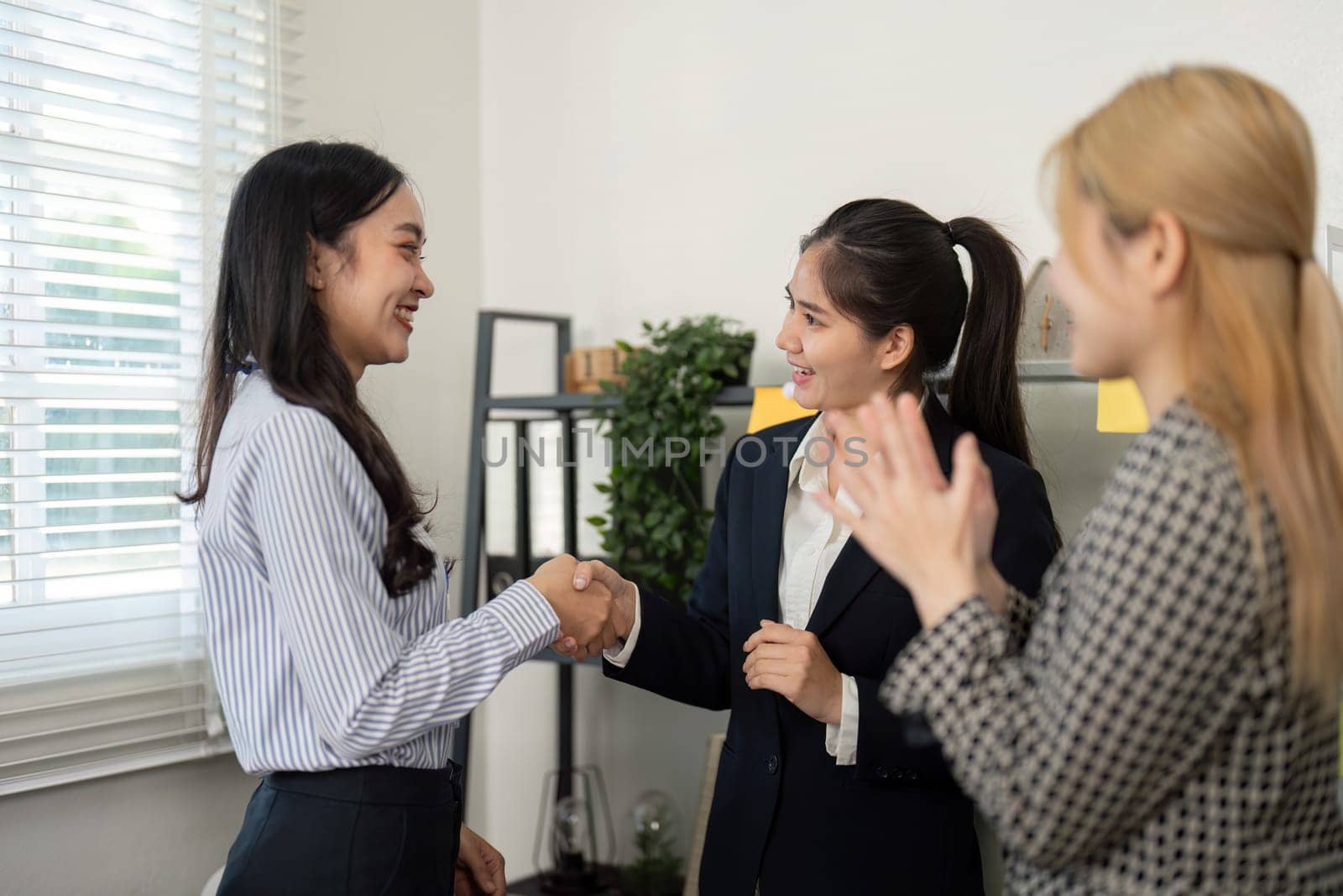 Two businesswomen shake hands while celebrating a successful partnership, highlighting teamwork and collaboration in the office.