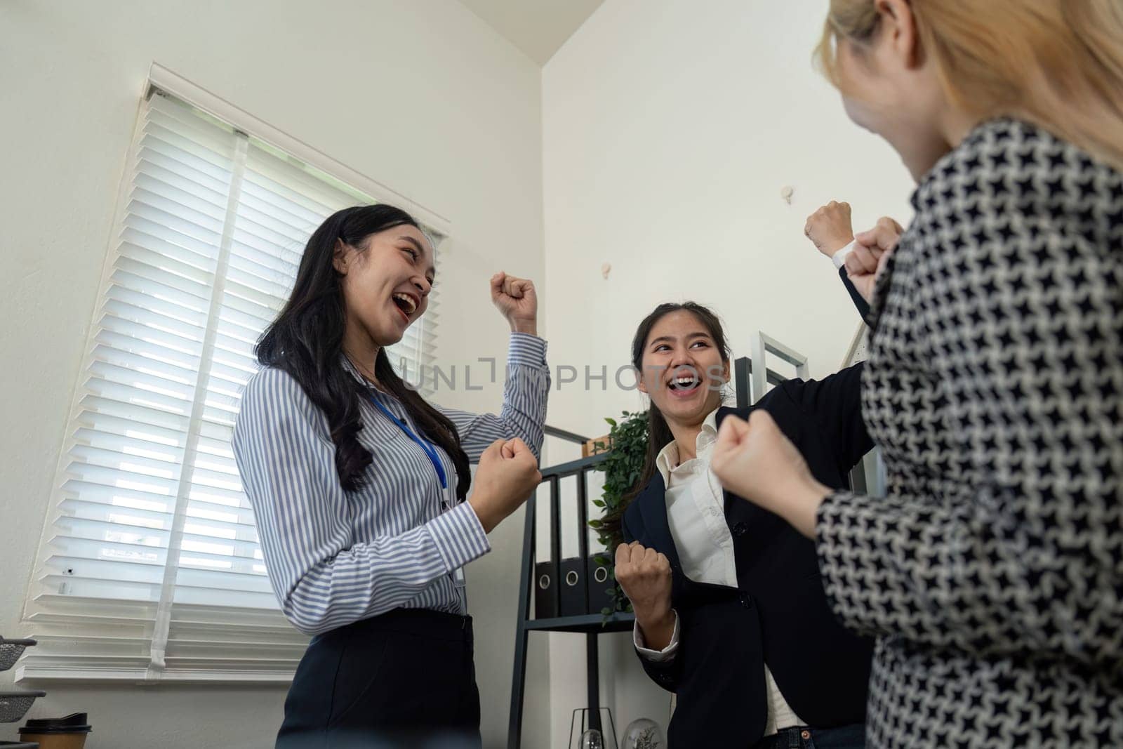 A diverse team of women celebrates a successful project in the office, showcasing teamwork and enthusiasm.