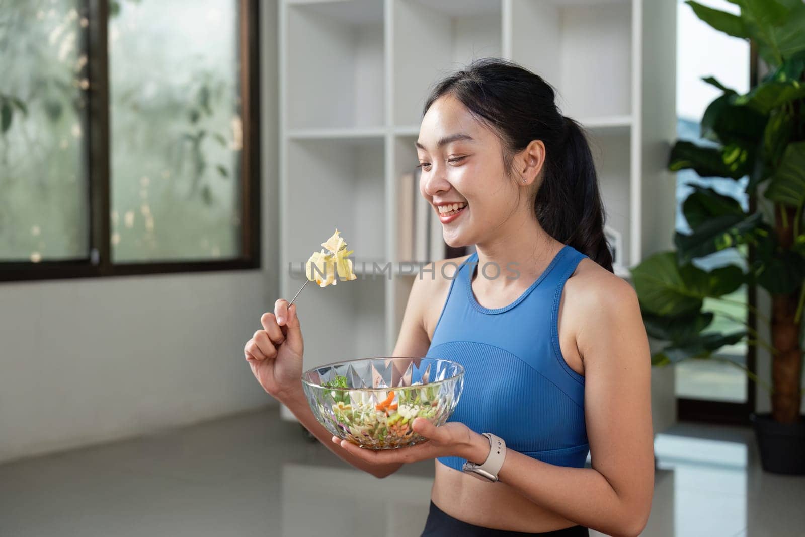 A cheerful woman holds a vibrant salad bowl, celebrating healthy eating and nutrition in a lively indoor space.