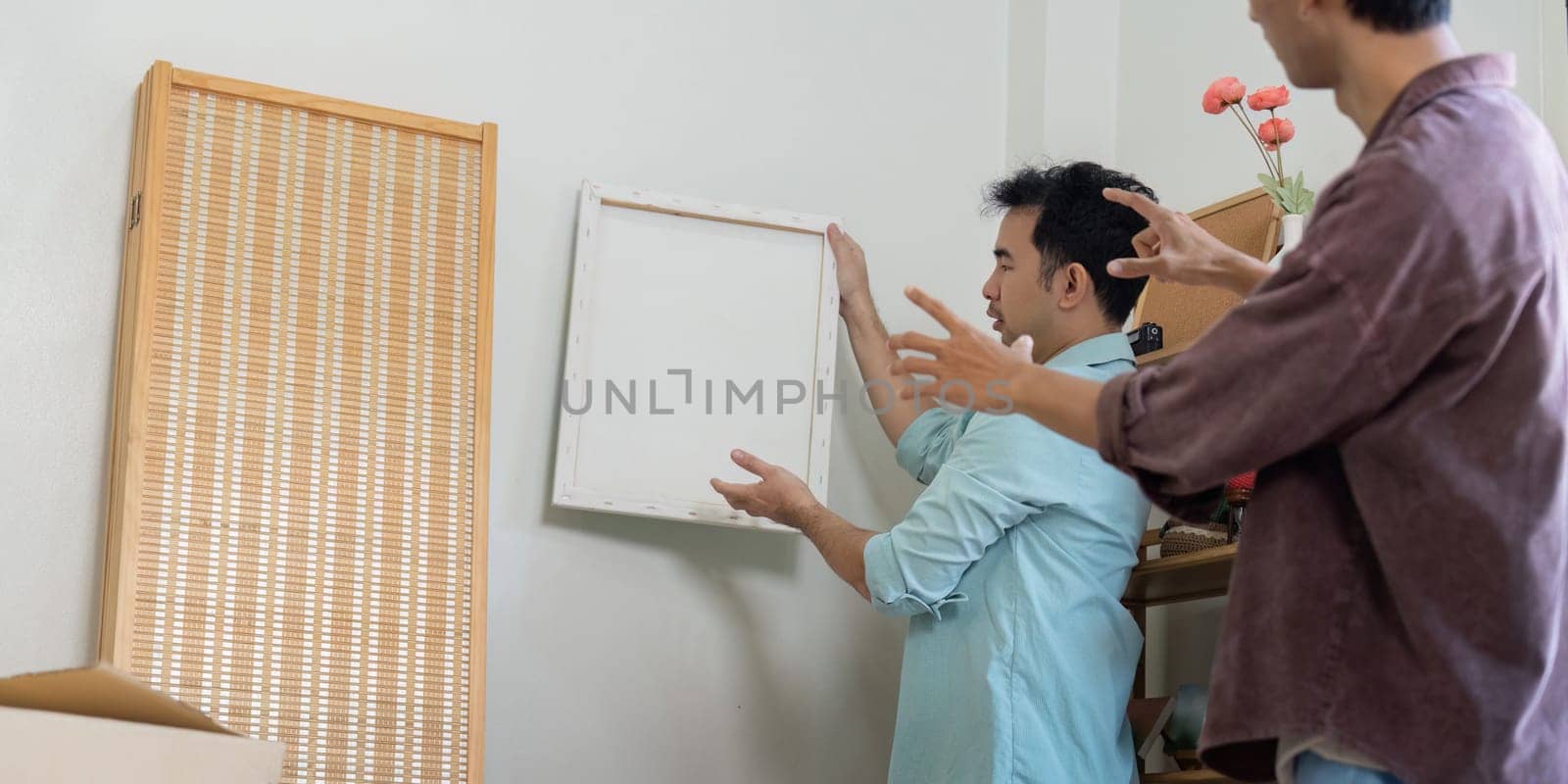 A joyful gay couple discusses wall decor while preparing to move into their new home, showcasing love and collaboration.