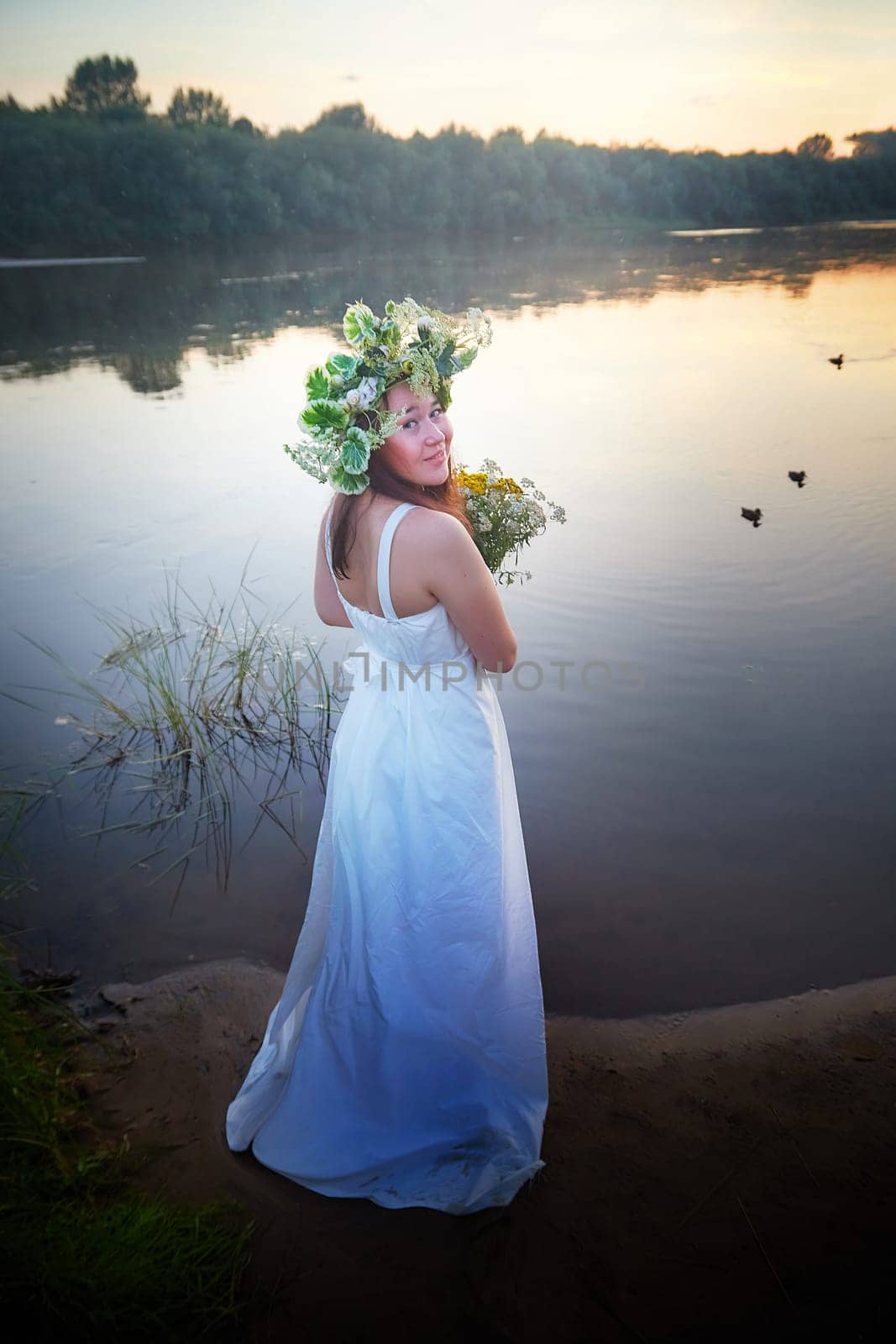 Young plump Girl in White Sundress With Flower Wreath in Water at Sunset Celebrating Ivan Kupala Holiday