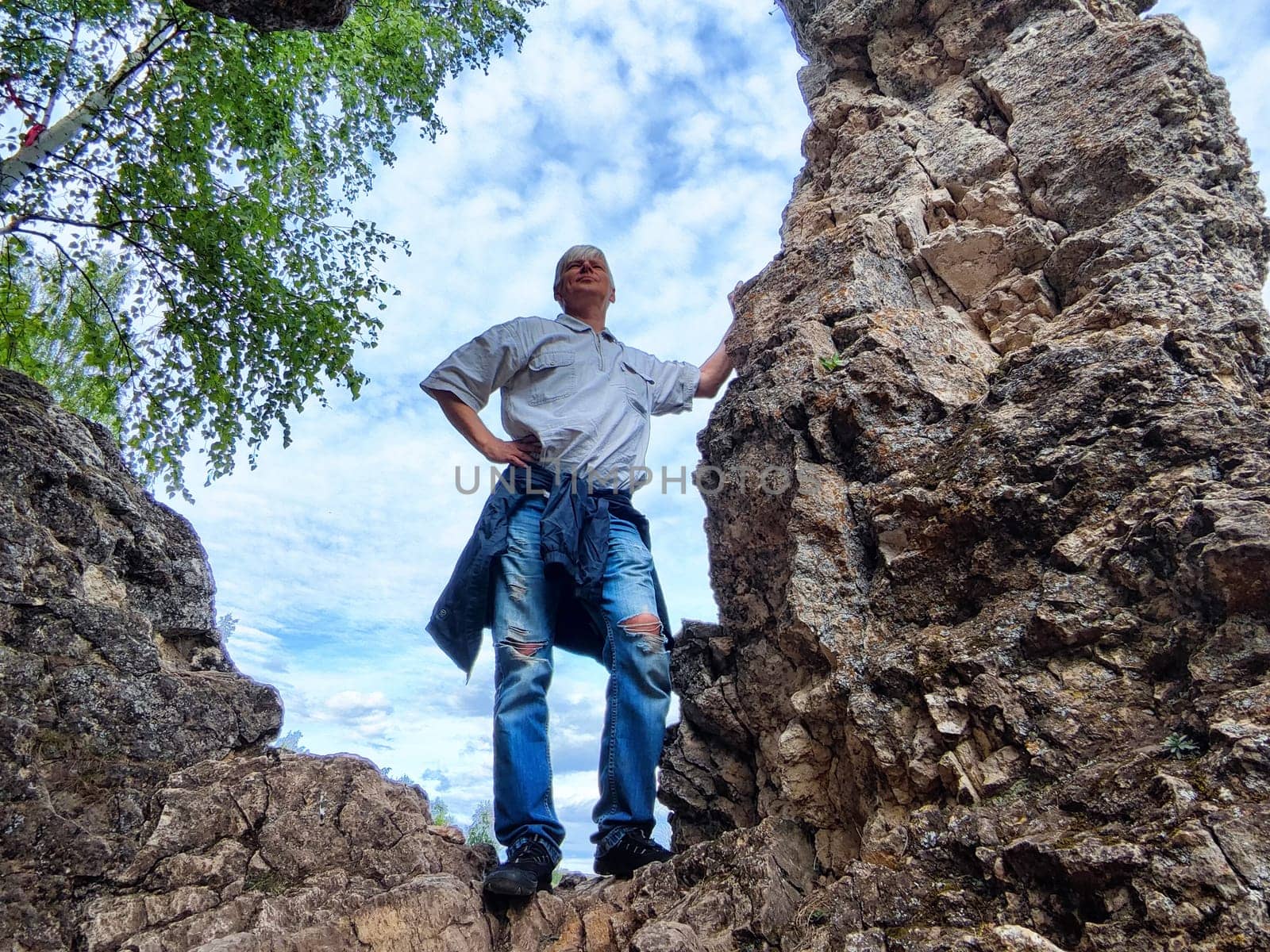 Individual poses confidently among rugged cliff formations, gazing into the distance on a pleasant day.