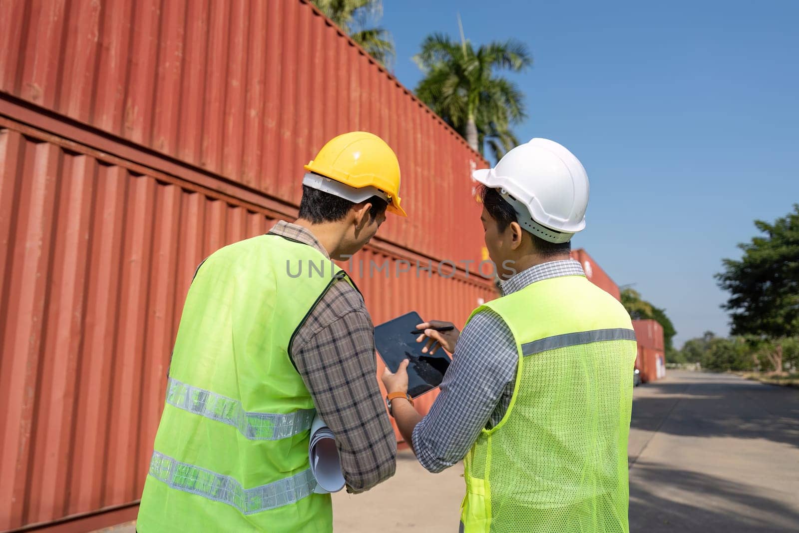 Engineers engage in discussion about logistics operations, reviewing plans in a shipping yard setting.