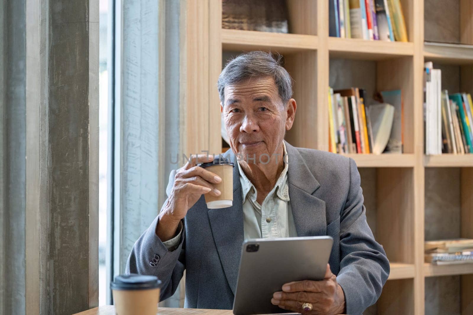 An elderly businessman sips coffee and engages with a tablet, showcasing a blend of technology and tradition in a cozy cafe.