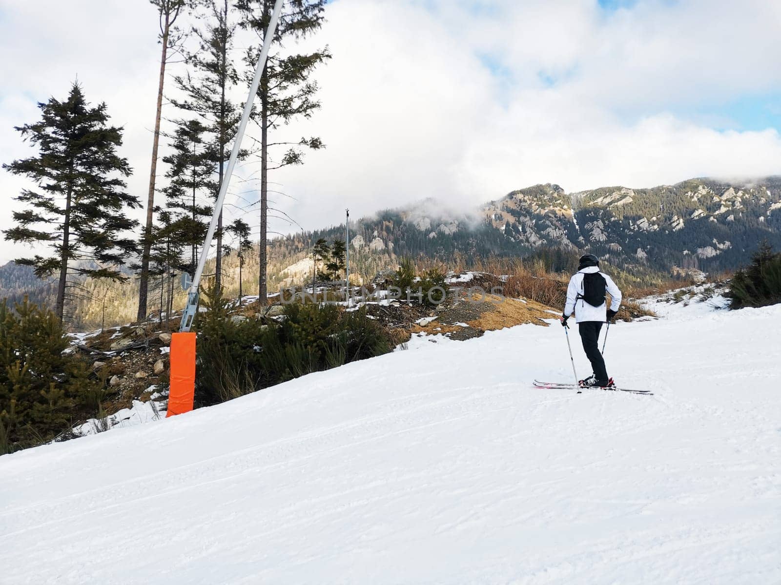 Man in ski suit and equipment stands on mountain slope. Ski run with skier. Beautiful view of the mountains, winter landscape with snow