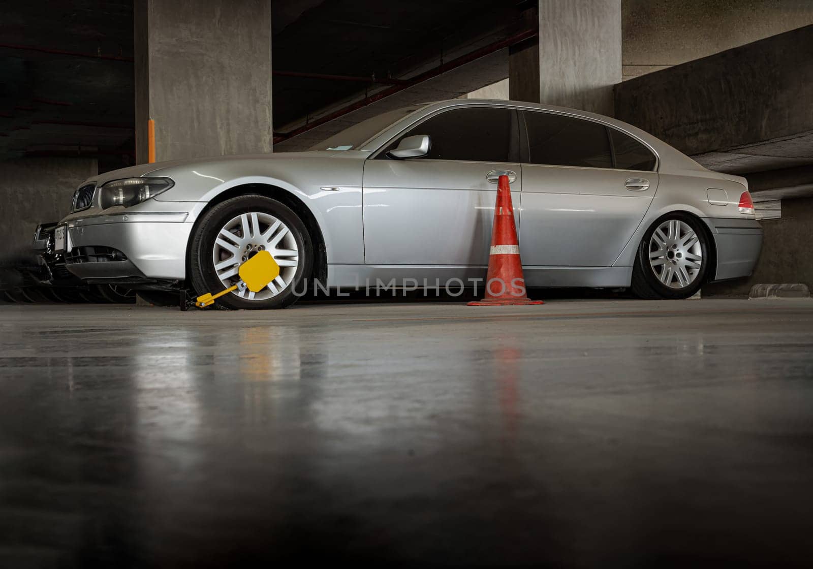 Bangkok, Thailand - Jan 18, 2025 - View of Car wheel blocked by wheel lock and traffic cone because illegal parking violation in parking lot of condominium building. use it as your wallpaper, poster and space for text, selective focus.