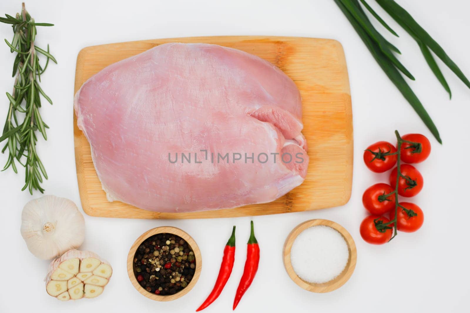 Top view in the center of a piece of turkey fillet brisket lying on a wooden cutting board on a white background surrounded by seasonings, herbs and vegetables. The concept of healthy eating, dietary and natural products, cooking. High quality photo