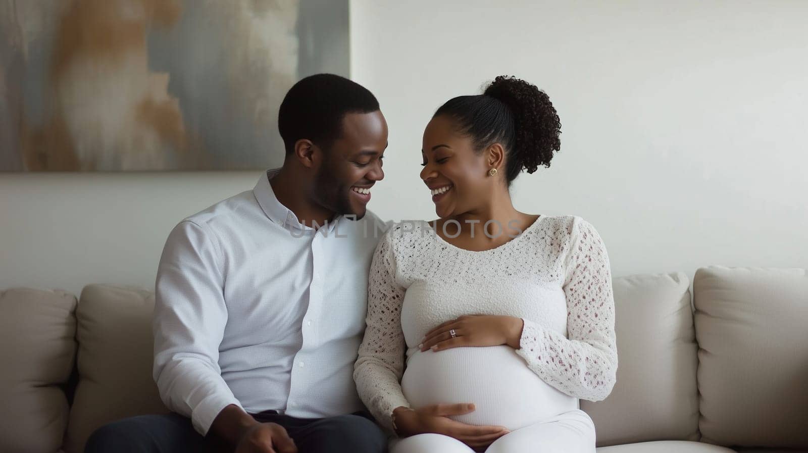 Happy pregnancy loving African couple, pregnant black American mother with belly and father smiling together sitting on sofa in living room at home