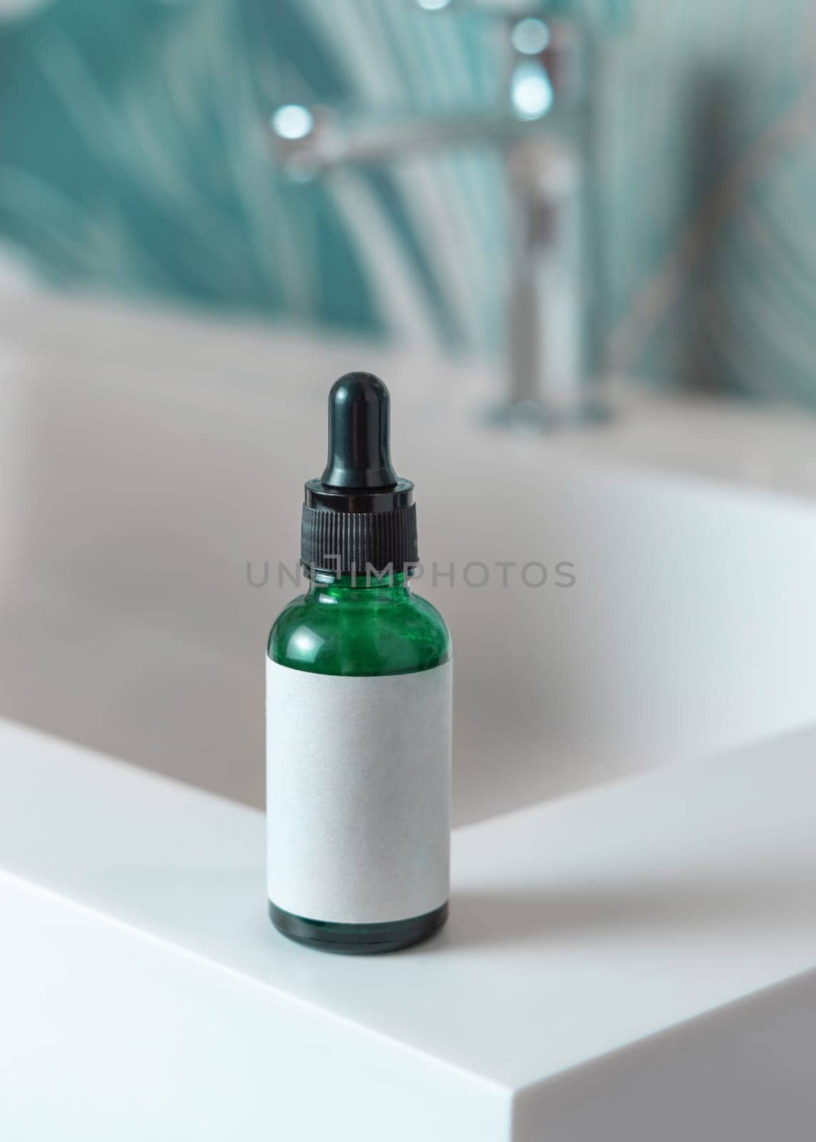 Green glass dropper bottle with pipette and blank label on washbasin with faucet in green tropical bathroom close up. Natural cosmetics - serum or essence. Daily beauty procedures