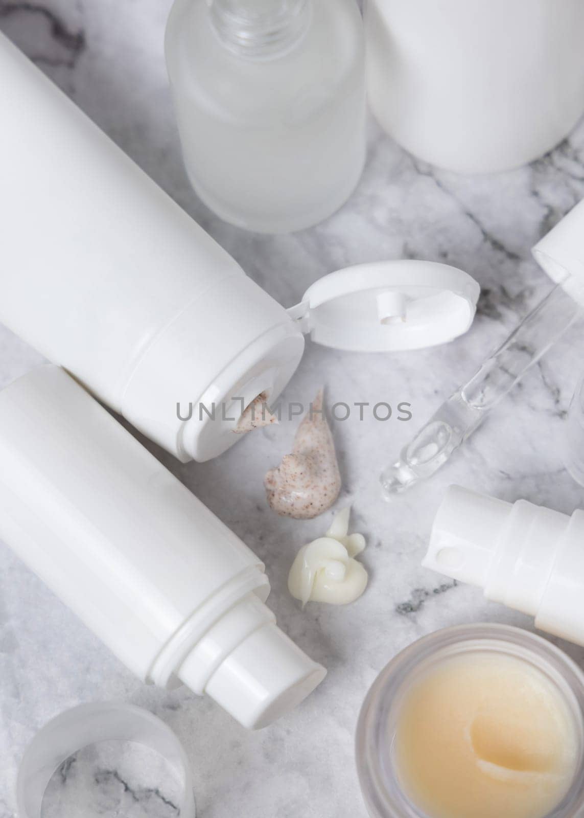 White opened cream tubes, bottles and jars on white marble table top view, mockup. Beige scrub and cream squeezed on table. Natural products for daily face care, spa procedures
