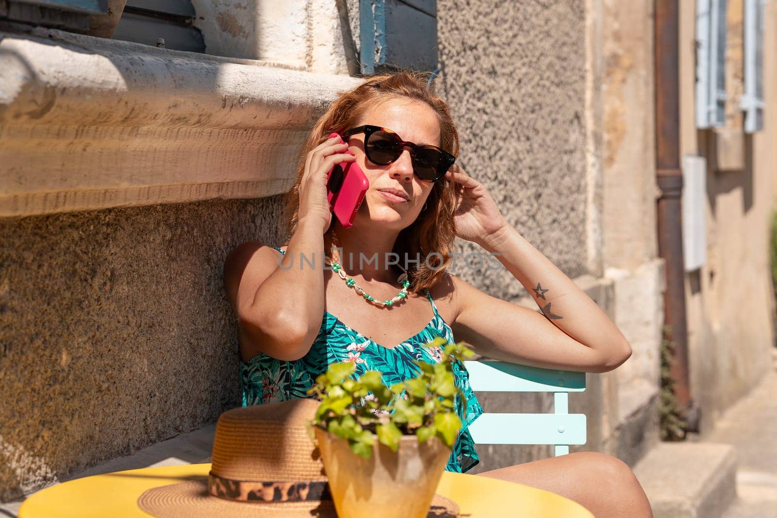 Beautiful young caucasian woman wearing sunglasses, having a conversation on a cell phone on a terrace of a cafe.
