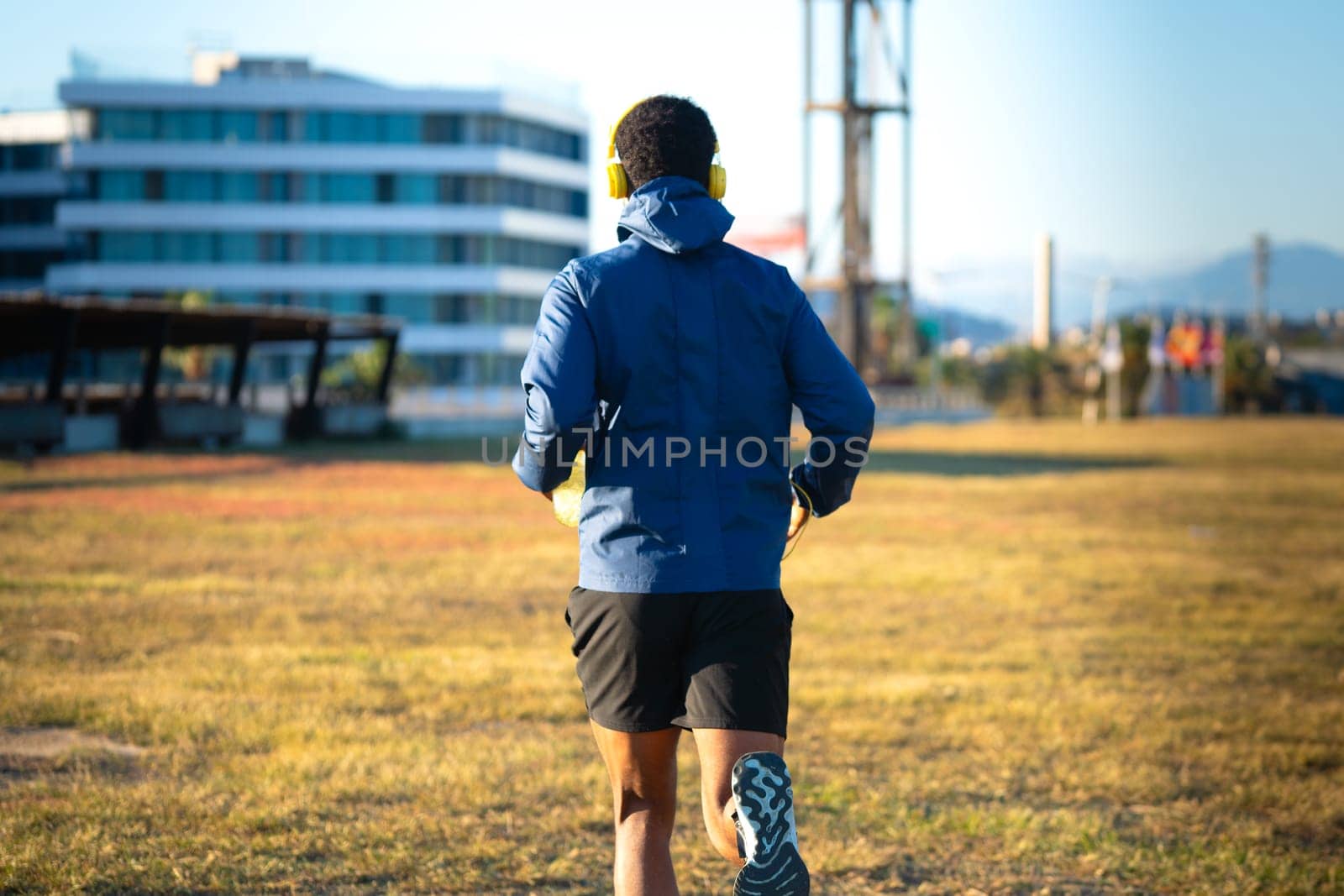 Young runner wearing headphones holding cold isotonic sports water in his hand