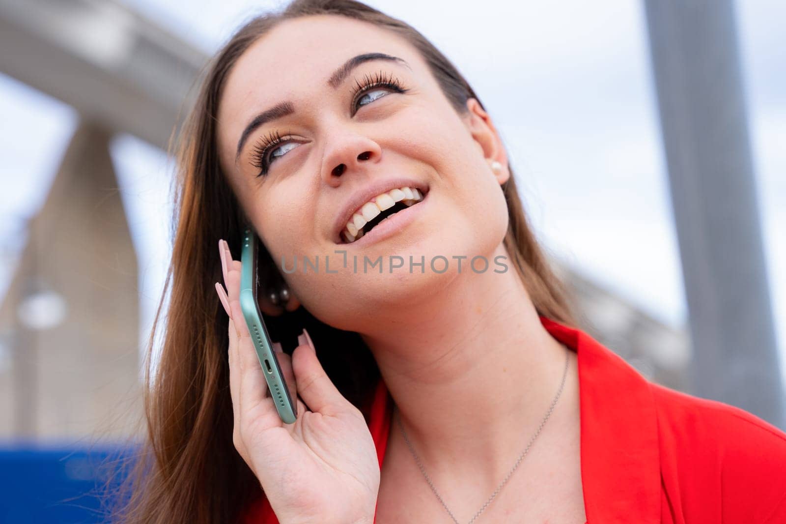 Smiling beautiful young businesswoman caucasian girl, wearing red jacket outdoors, chatting on cell phone