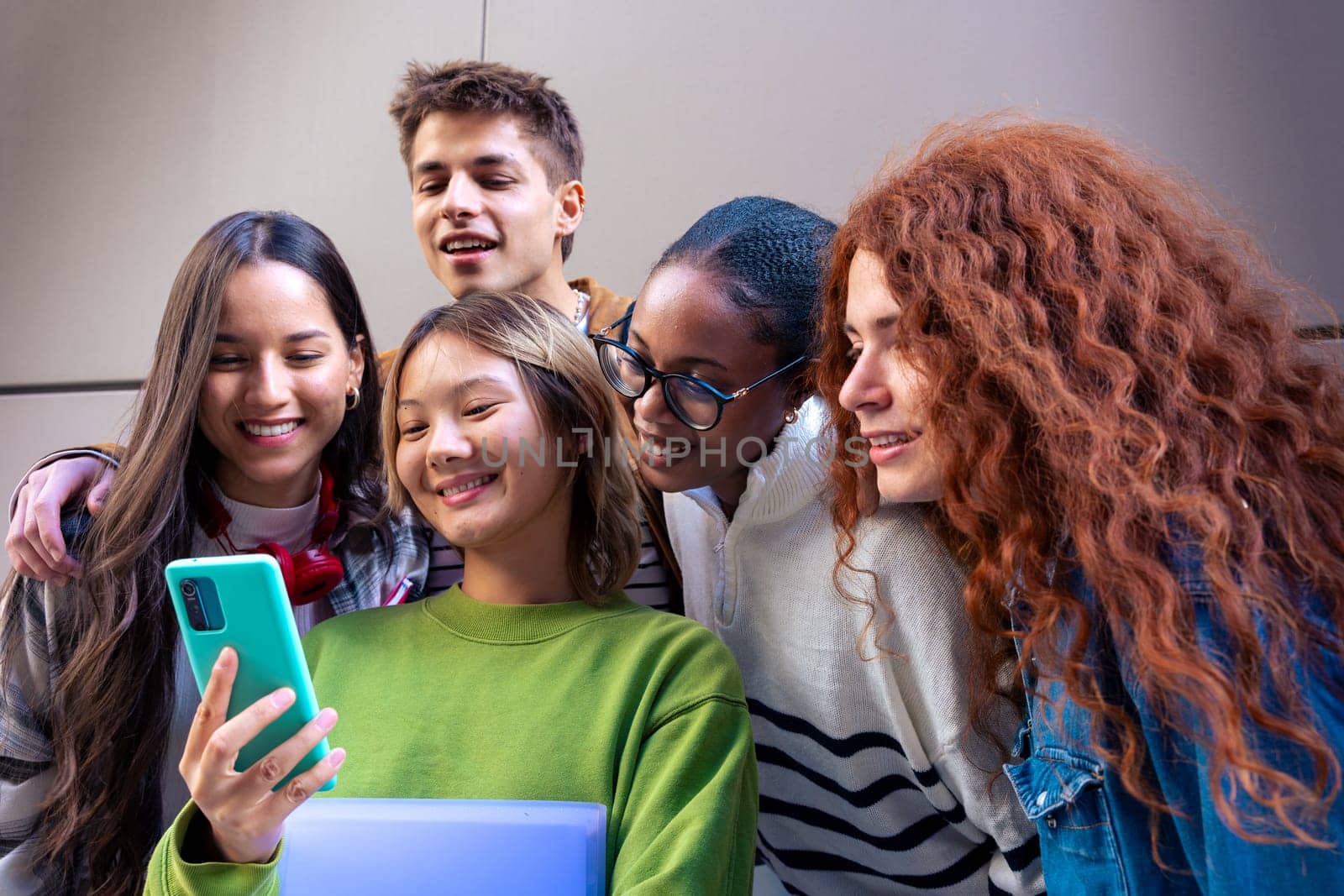 Five multiracial friends having fun using social media with their smartphone on the university campus. University life concept.
