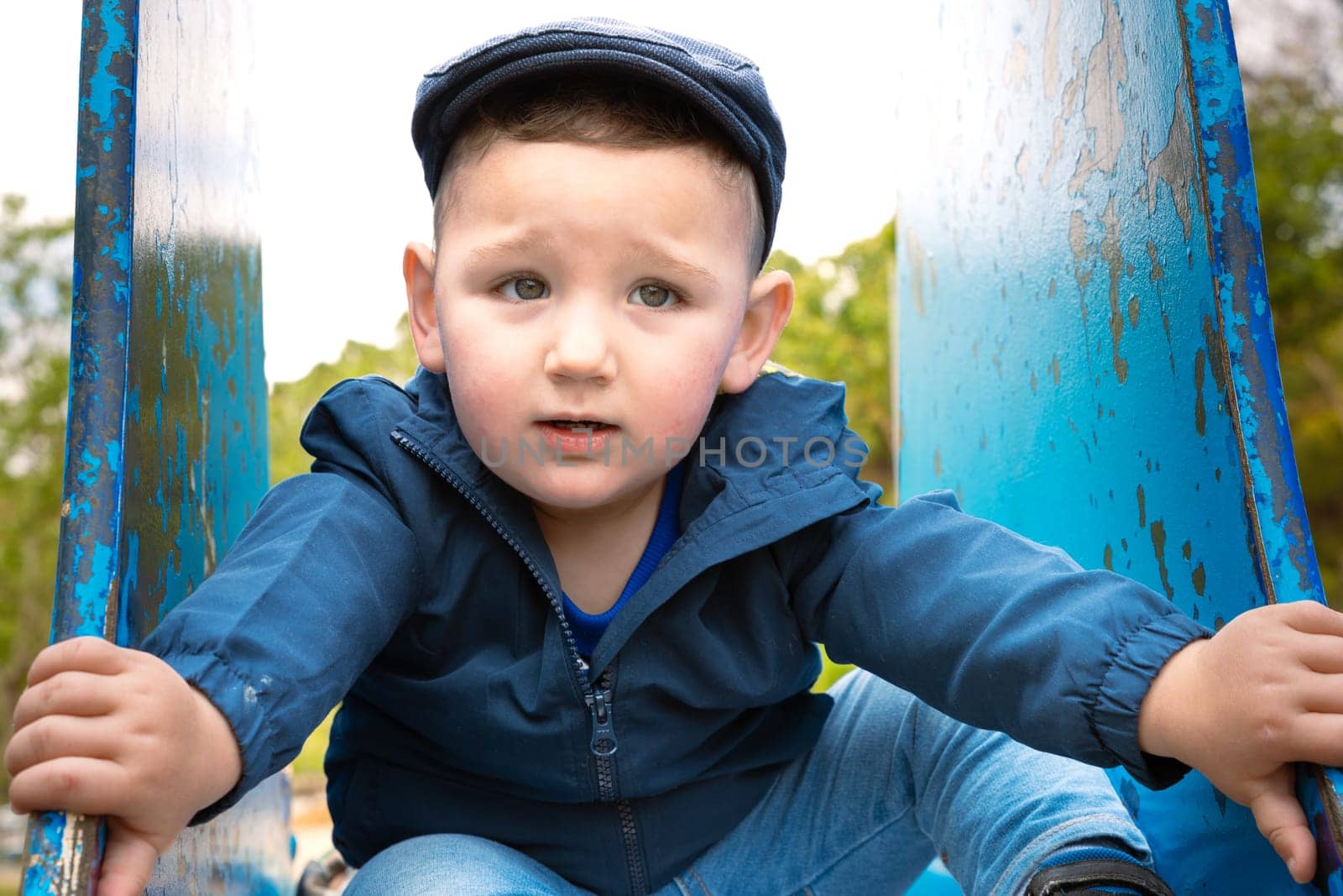 Sweet little Caucasian boy in cap having fun smiling widely sliding down the slide.