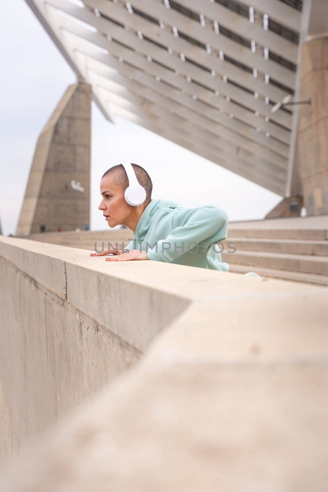 Sporty woman with sports headphones doing concentrated stretching outdoors.