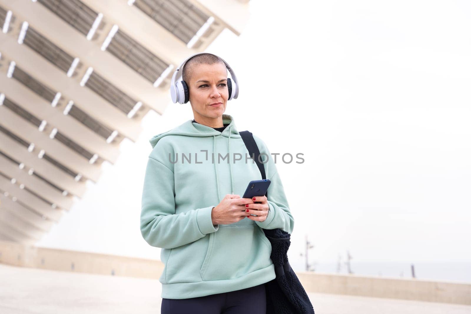 An athletic woman with headphones tired from exercising takes a break to use a cell phone messaging app.