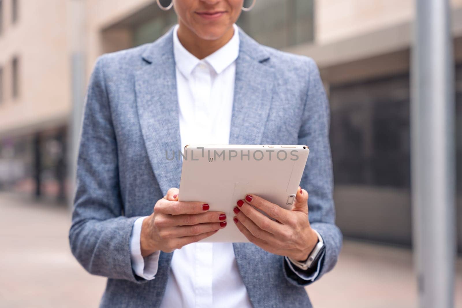 Thoughtful businesswoman with results of businesswoman walking down the street outside office building, a mature boss holds a phone in her hands, writes messages and reads news online, using an app.