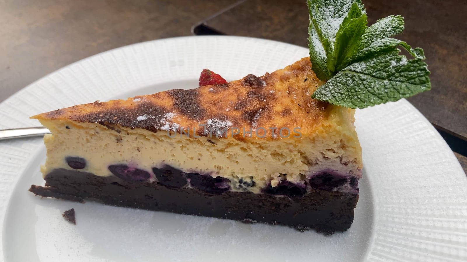 Delicious Slice of Blueberry Cheesecake With a Chocolate Crust, Topped With Fresh Mint and Powdered Sugar.