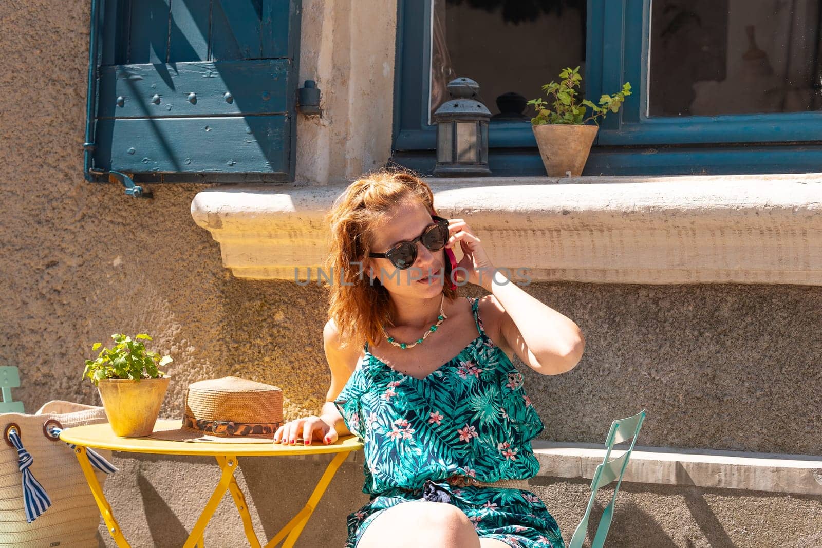 Beautiful young caucasian woman wearing sunglasses, having a conversation on a cell phone on a terrace of a cafe.