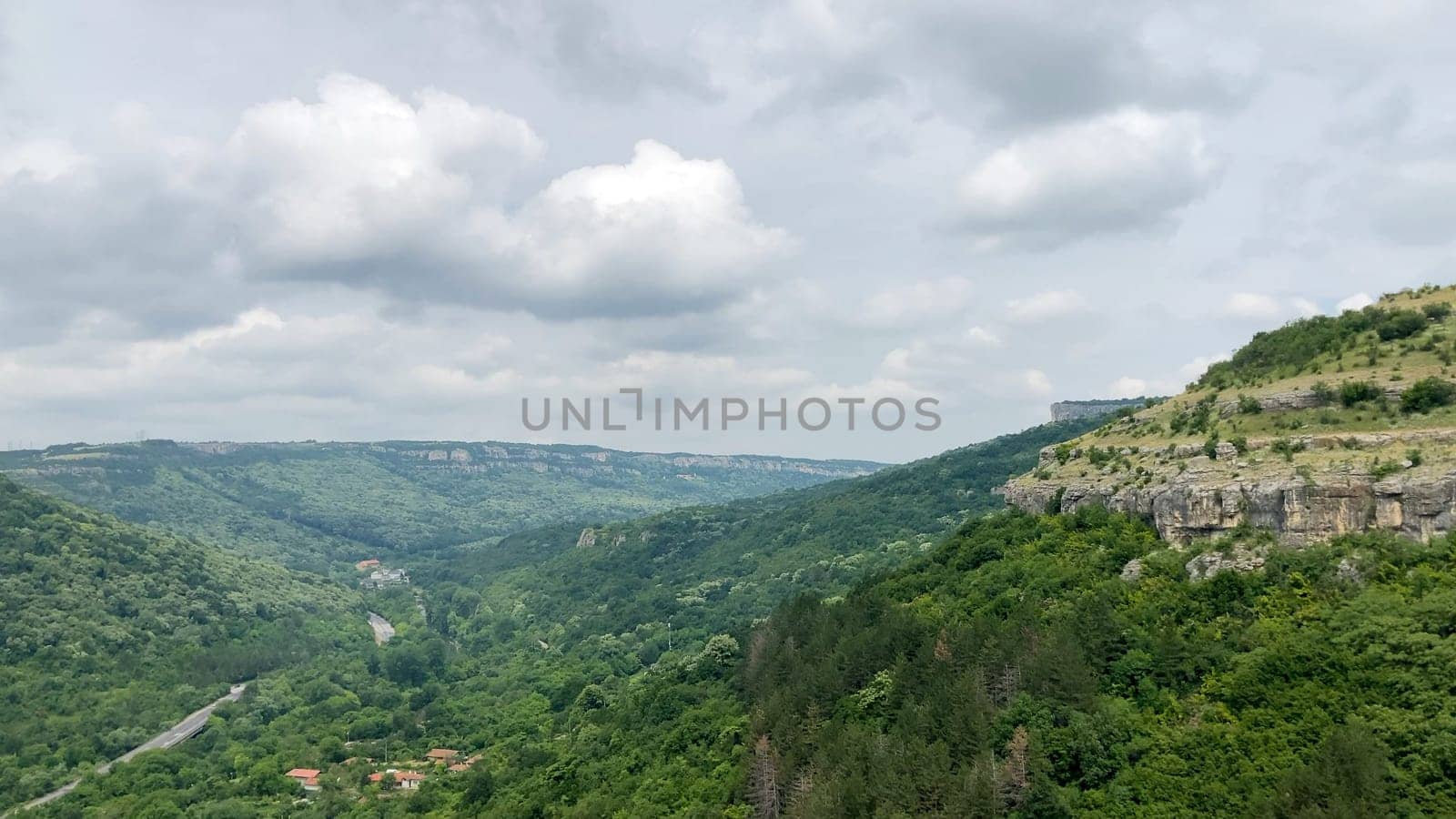 Scenic view of the Garga Bair Hill in Veliko Tarnovo, Bulgaria. Lush green valley with a winding road below. A cloudy sky overhead - Europe