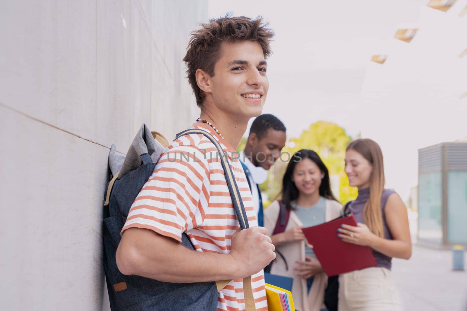Multiracial group of teenage students talking together about exam and homework. Happy teenager smiling taking a break standing on university campus holding backpack.